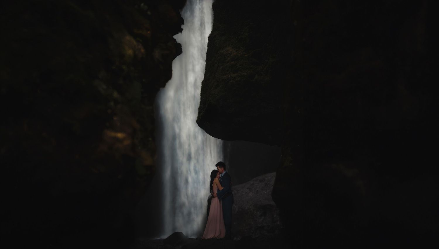 Moody silhouette of figures against dark cave wall with waterfall in background.