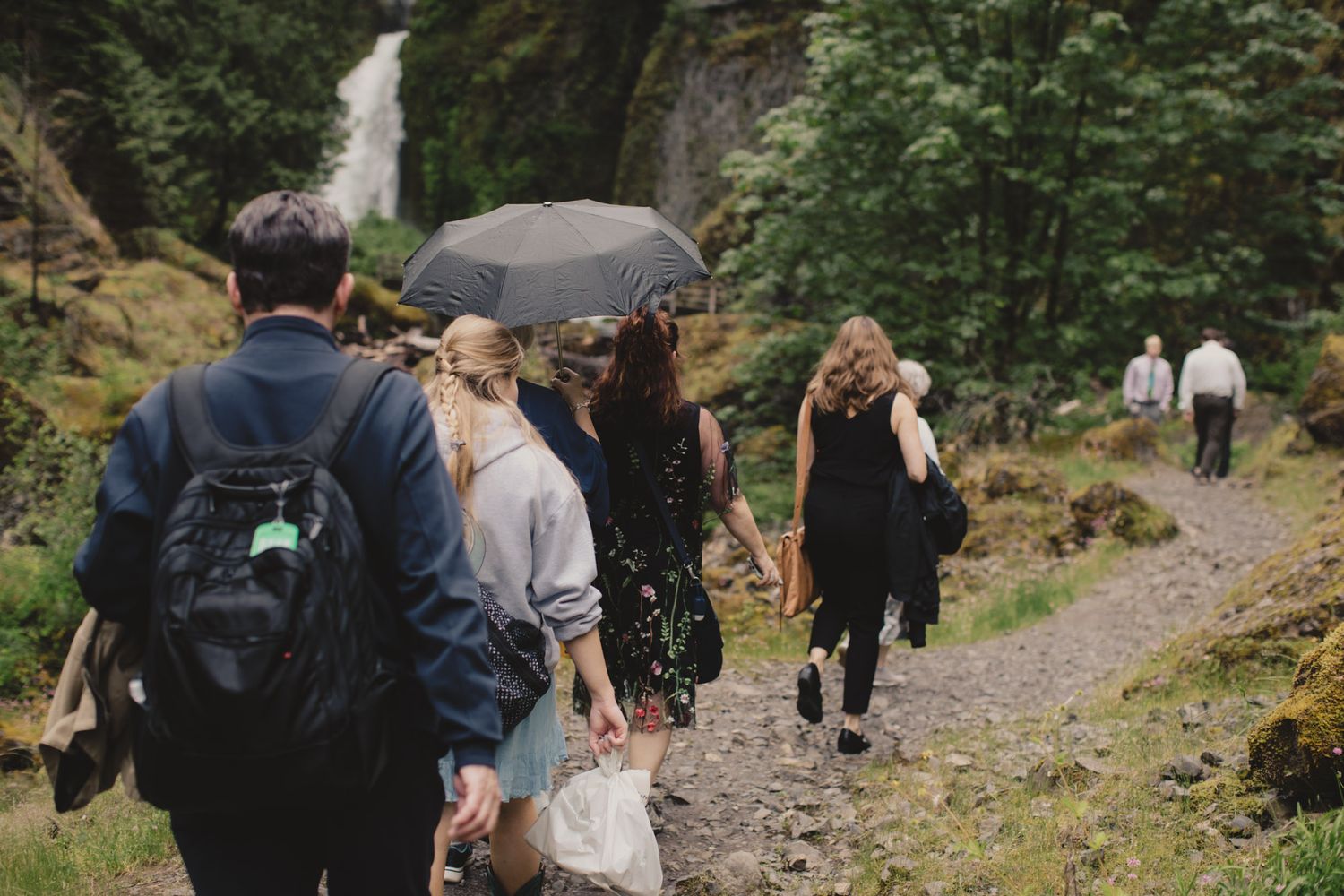 Group hiking along a nature trail with umbrellas near a scenic waterfall.