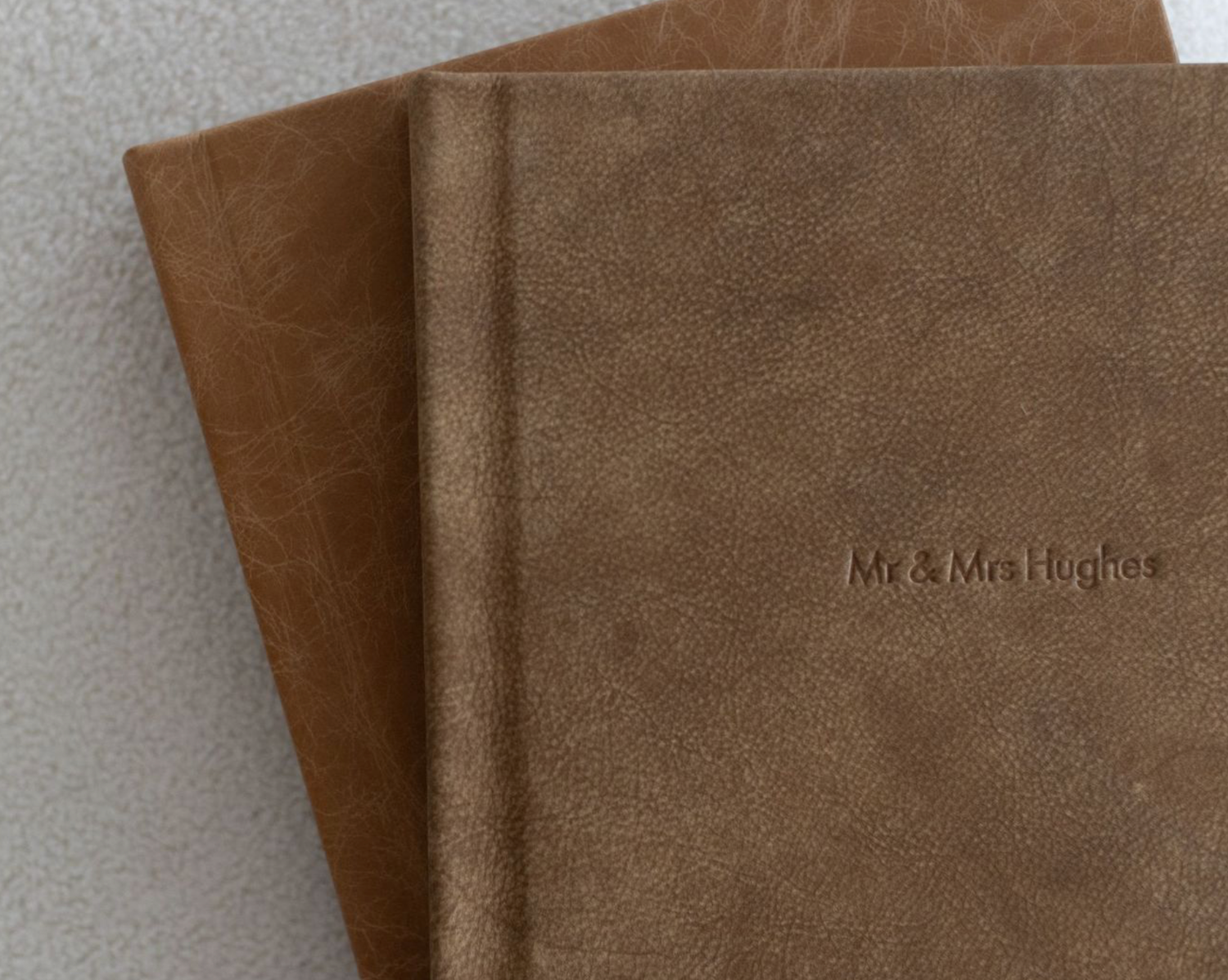 Two brown leather-bound photo albums stacked, with Mr & Mrs Hughes embossed on the top cover.