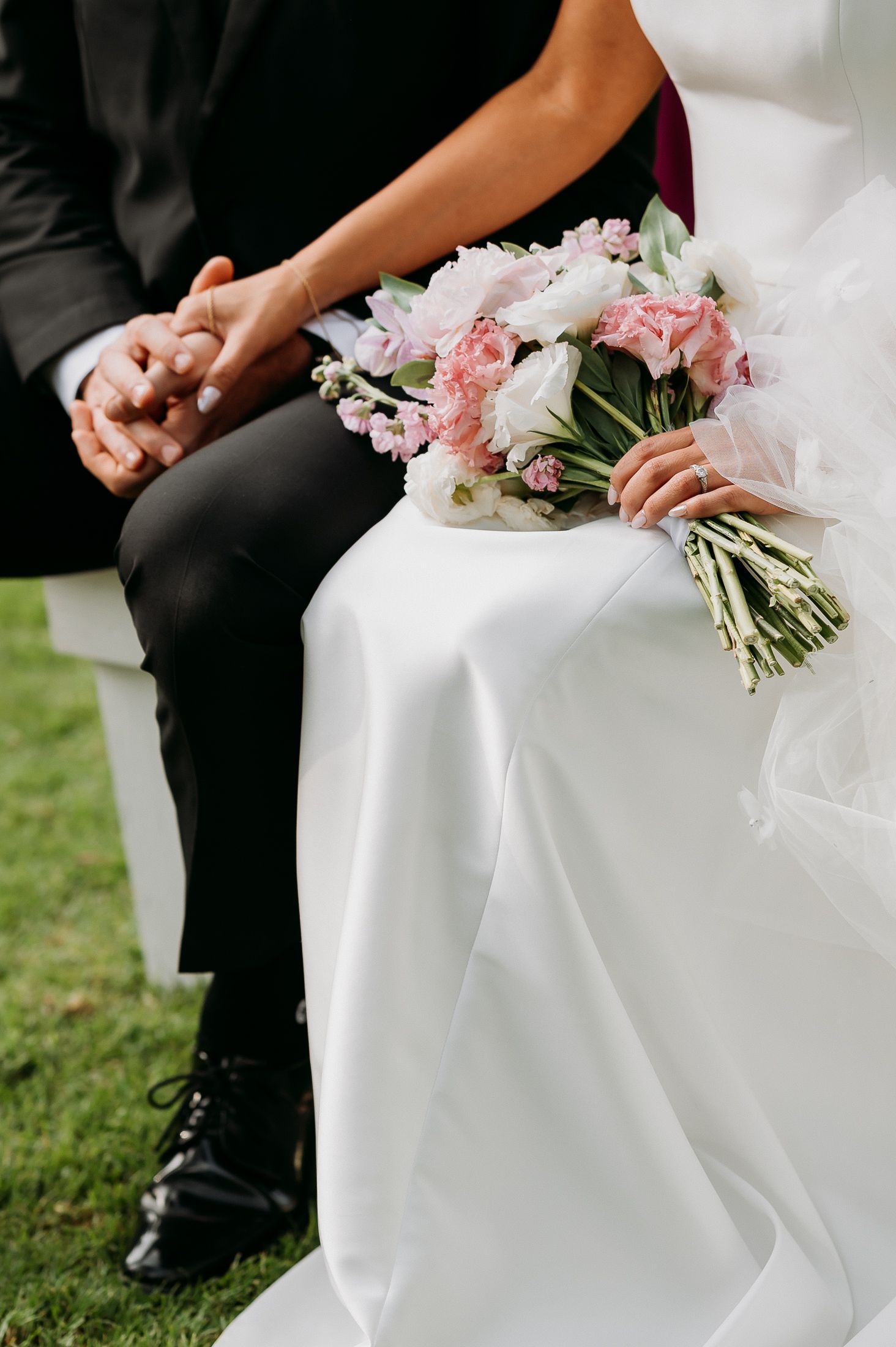 Bride holding pink and white floral bouquet while holding hands with groom during ceremony.