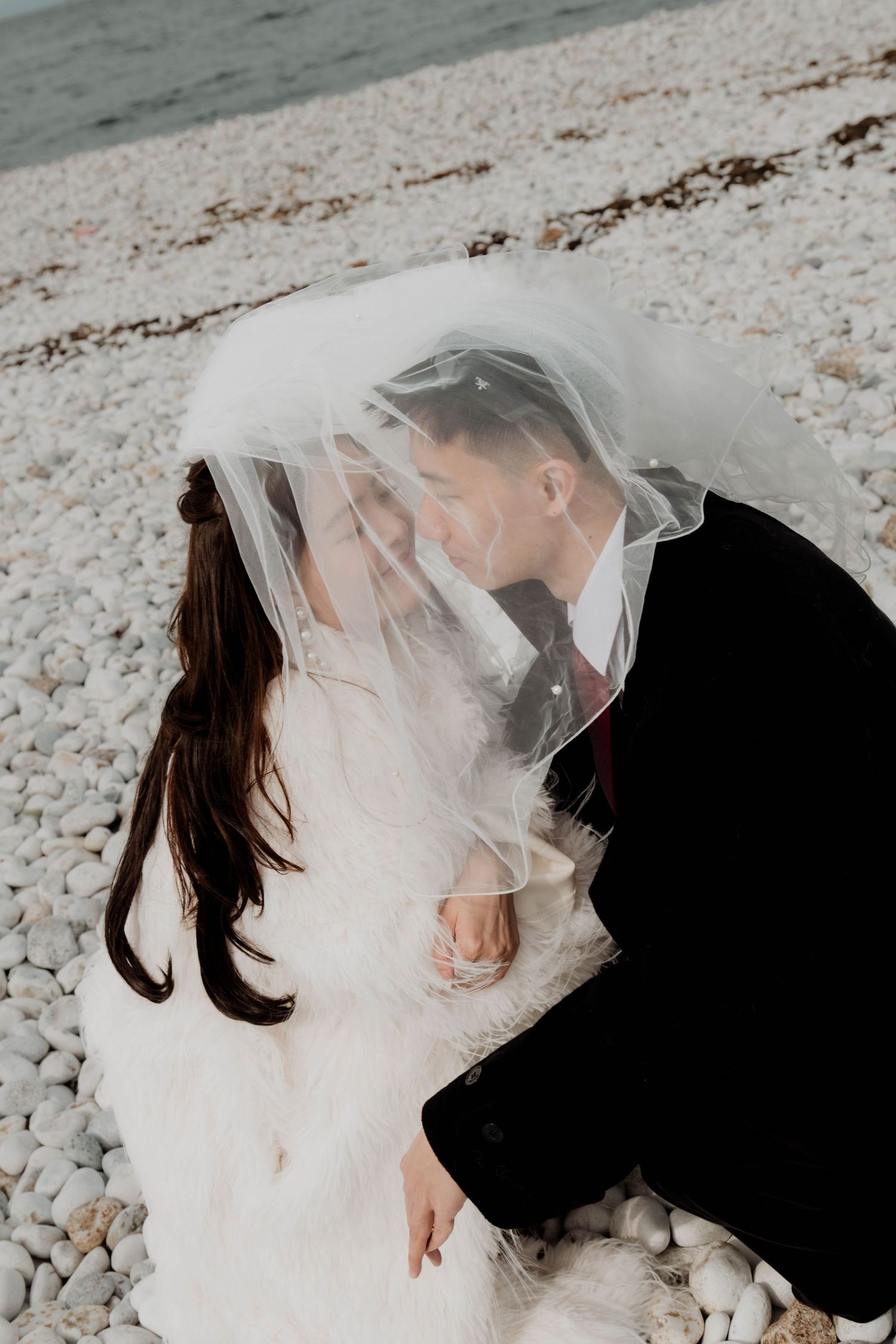Destination pre-wedding photoshoot Romantic wedding photo of couple under veil on rocky beach in Japan