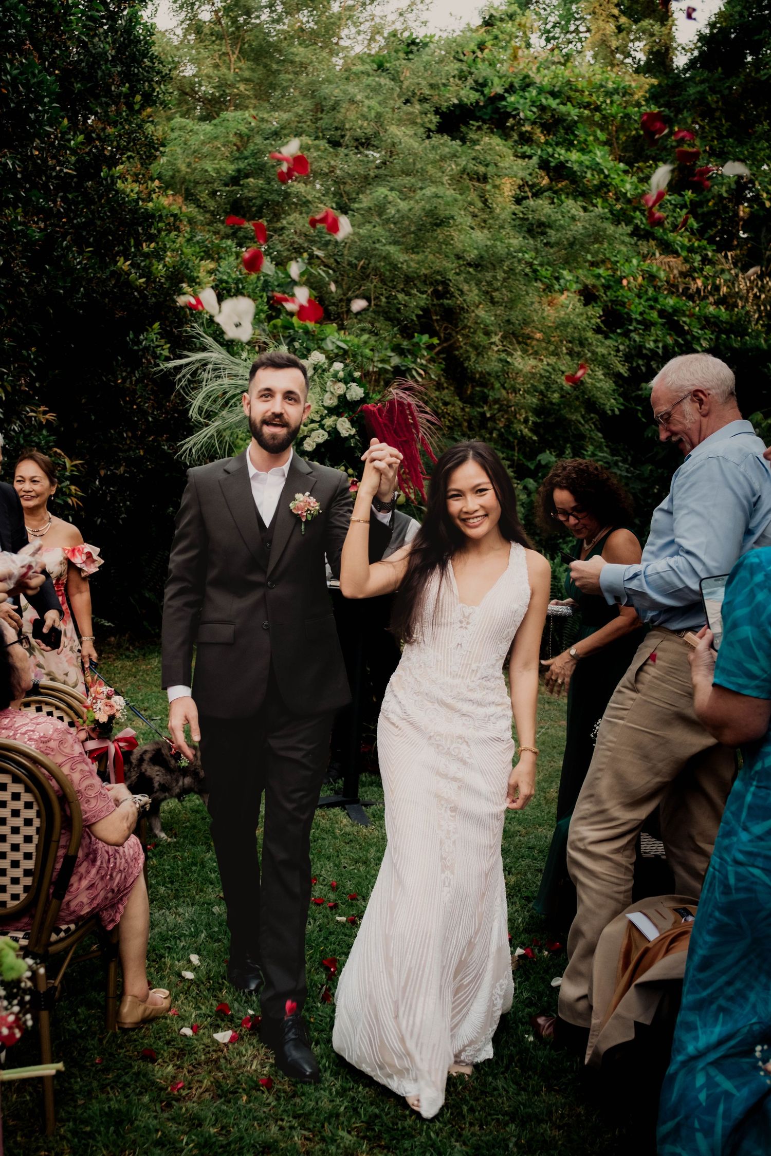 A garden wedding celebration with red roses and greenery as guests gather outdoors for the ceremony.