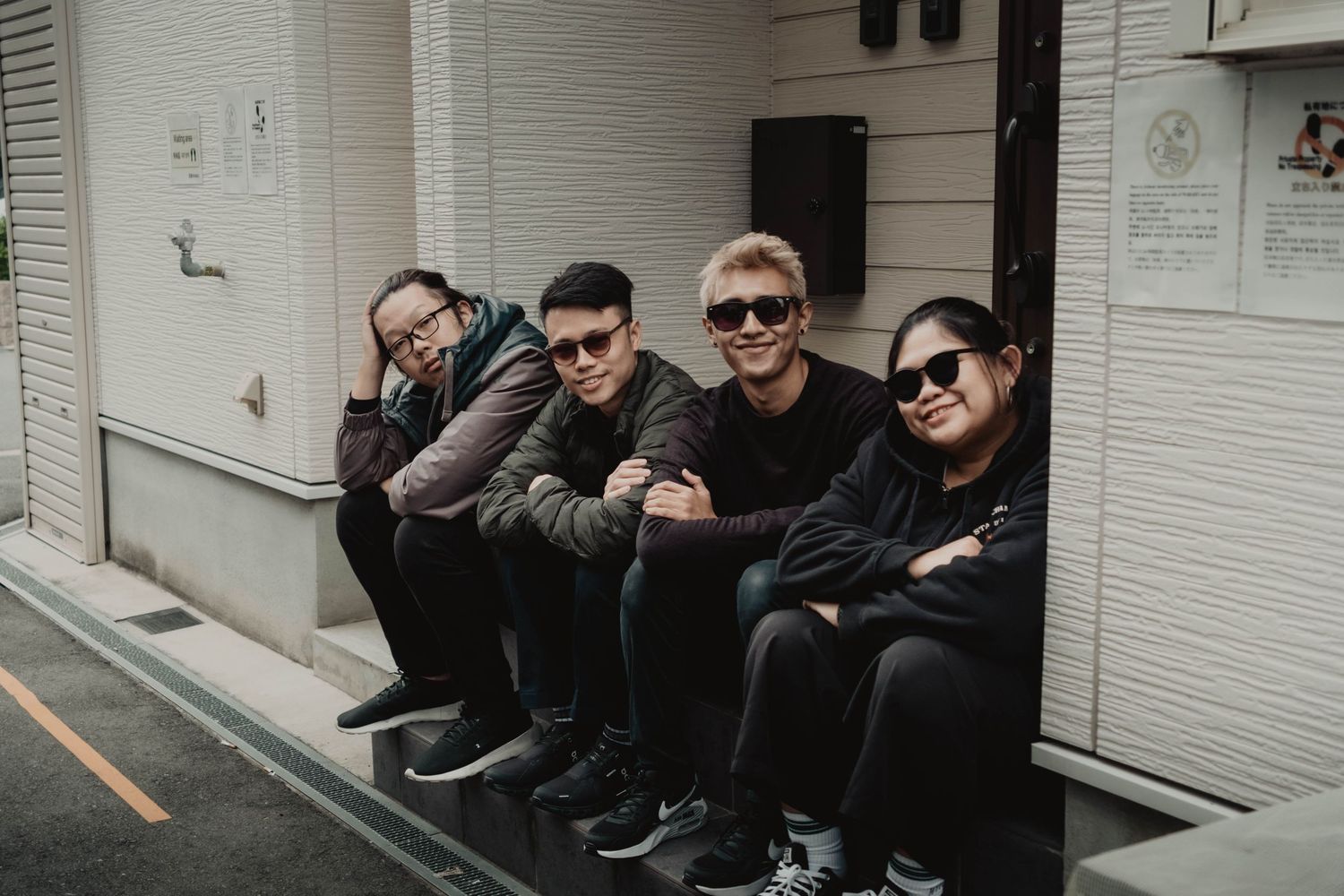 Memory Makers team - Friends in dark clothing sitting casually on steps against white building exterior in Japan.