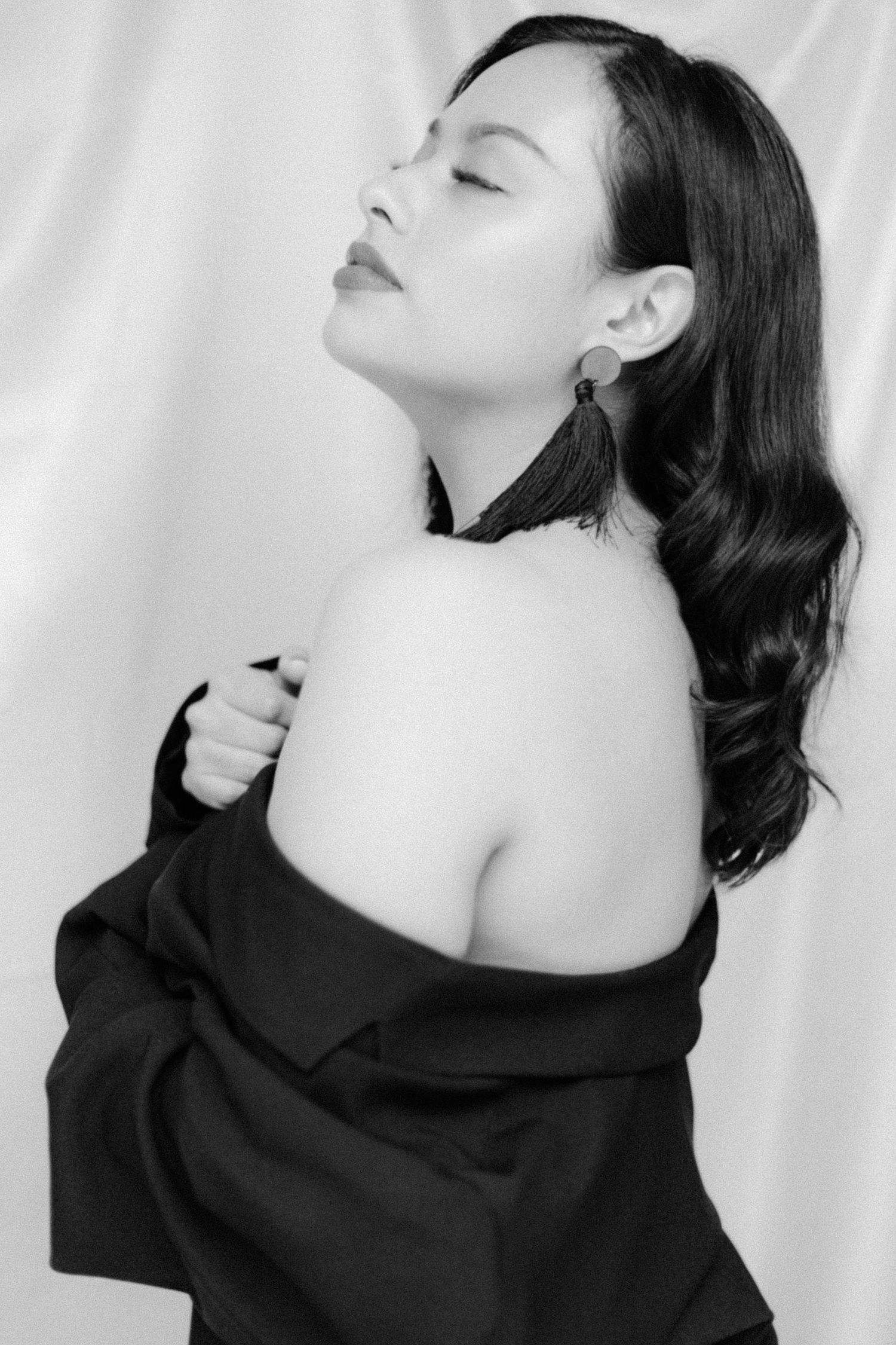 Dramatic black and white photo of person with flowing hair in off-shoulder garment against white backdrop.