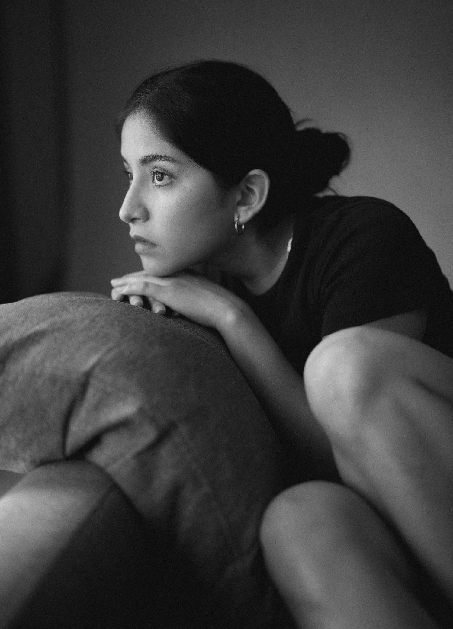 Moody black and white portrait of someone resting their head on a couch in contemplation.