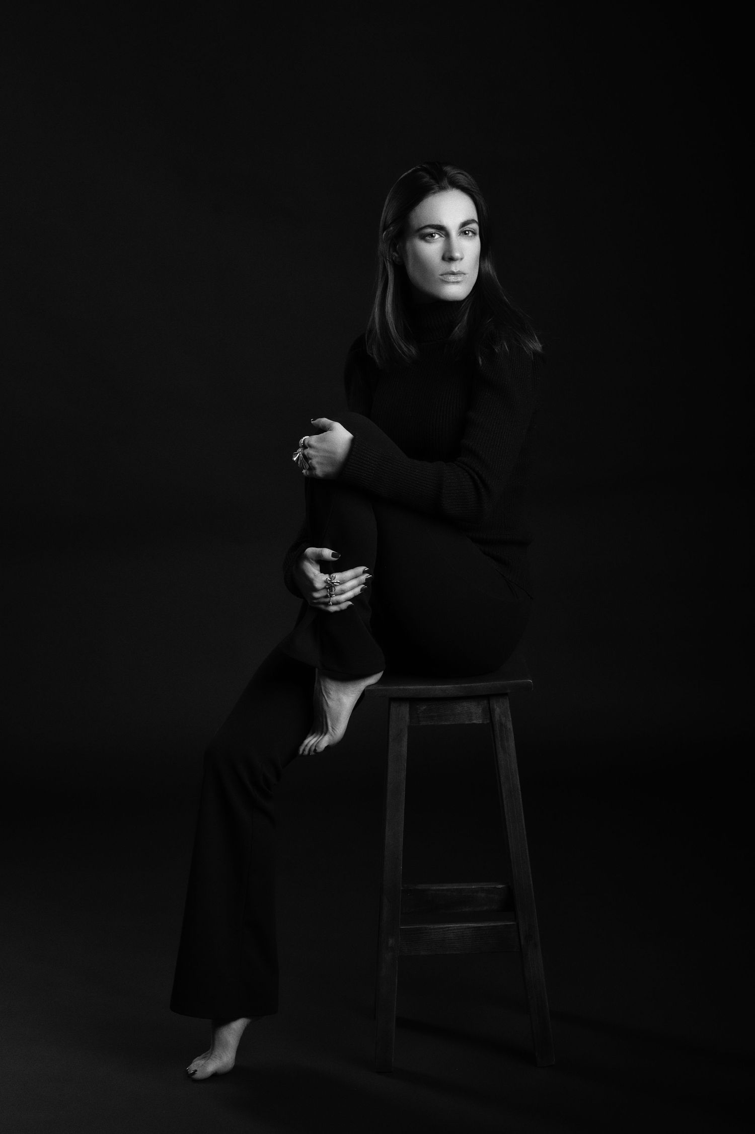 A dramatic black and white portrait series showing a person in dark clothing posed on a chair against a black background.