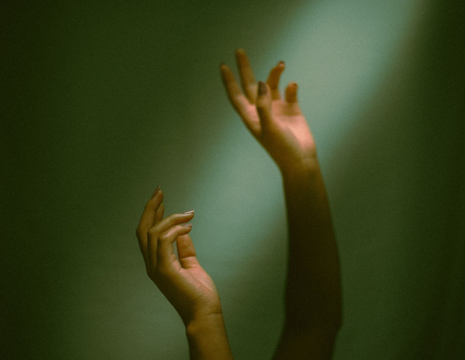 Artistic photograph of raised hands silhouetted against a moody green background.