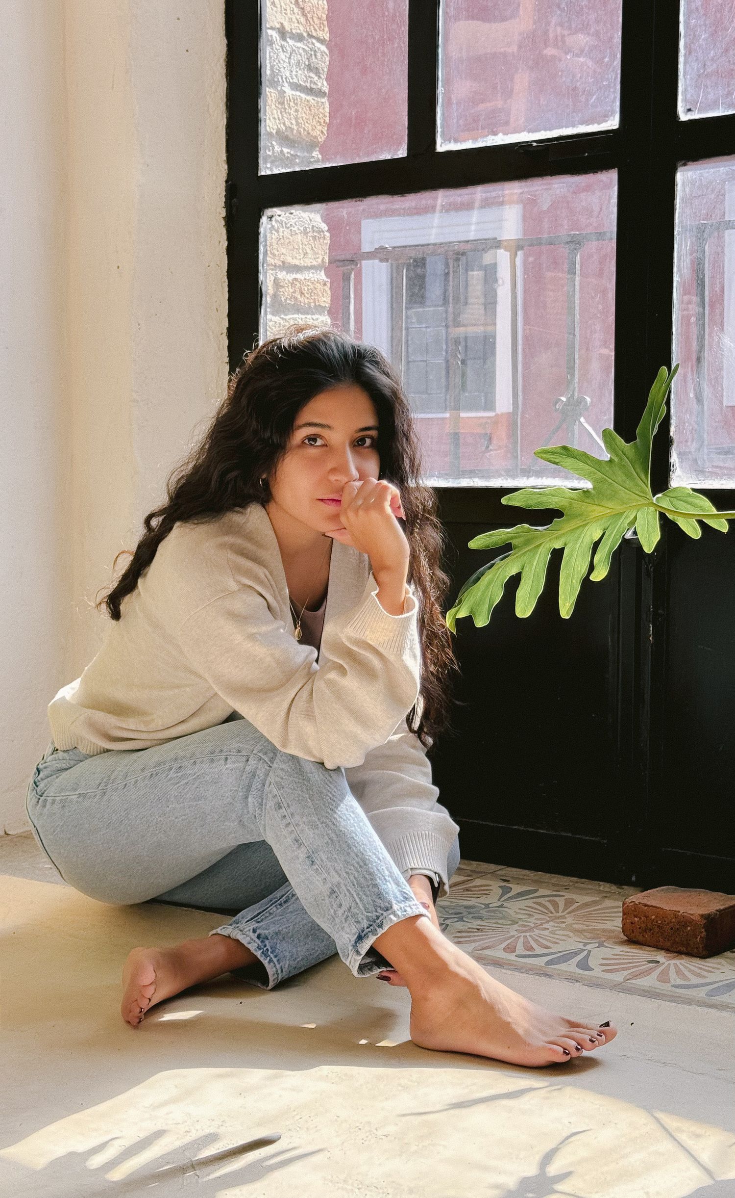 Young woman sitting casually by window with houseplant in natural light.