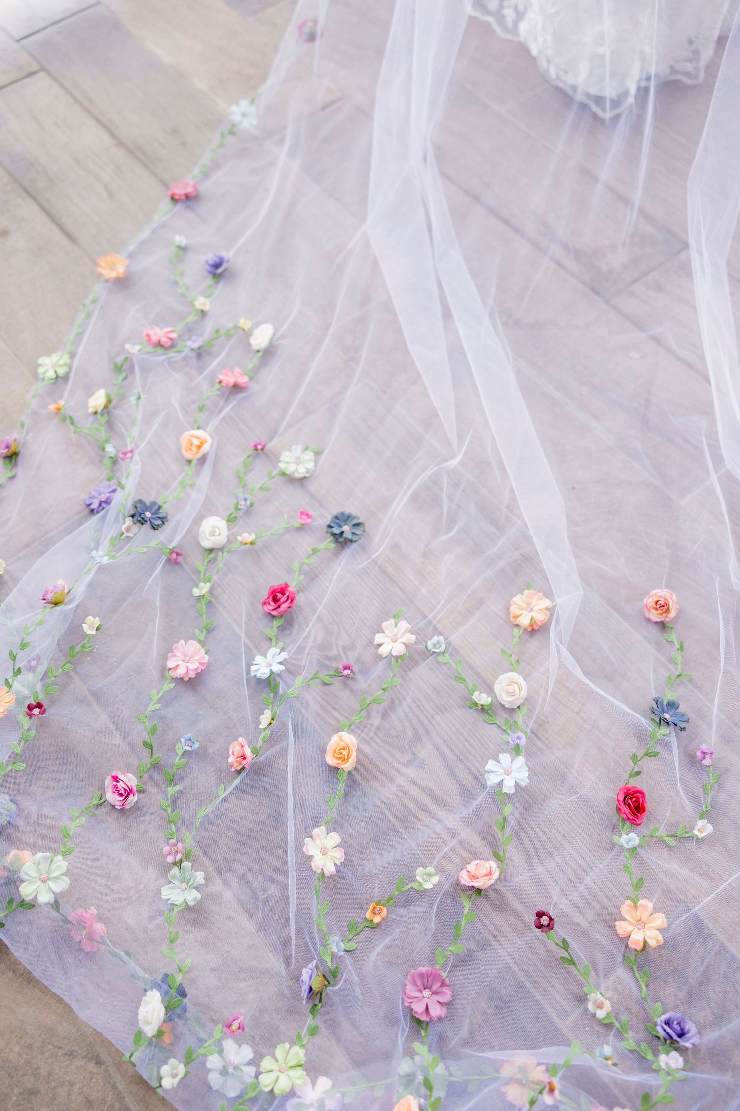 Delicate sheer tulle veil decorated with colorful small floral embellishments laid out on wooden flooring.