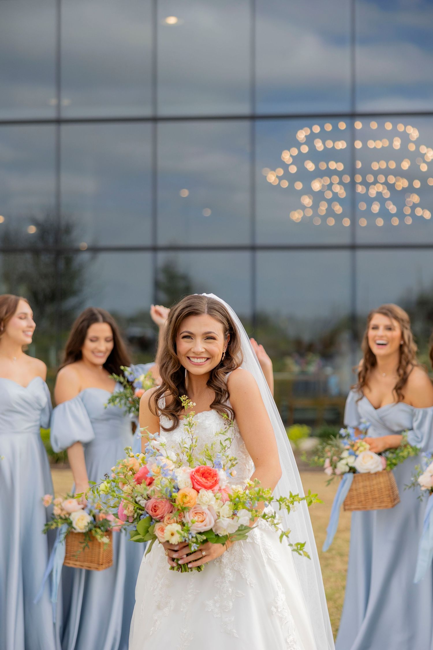 Wedding party in pale blue dresses posing outdoors with string lights in background.