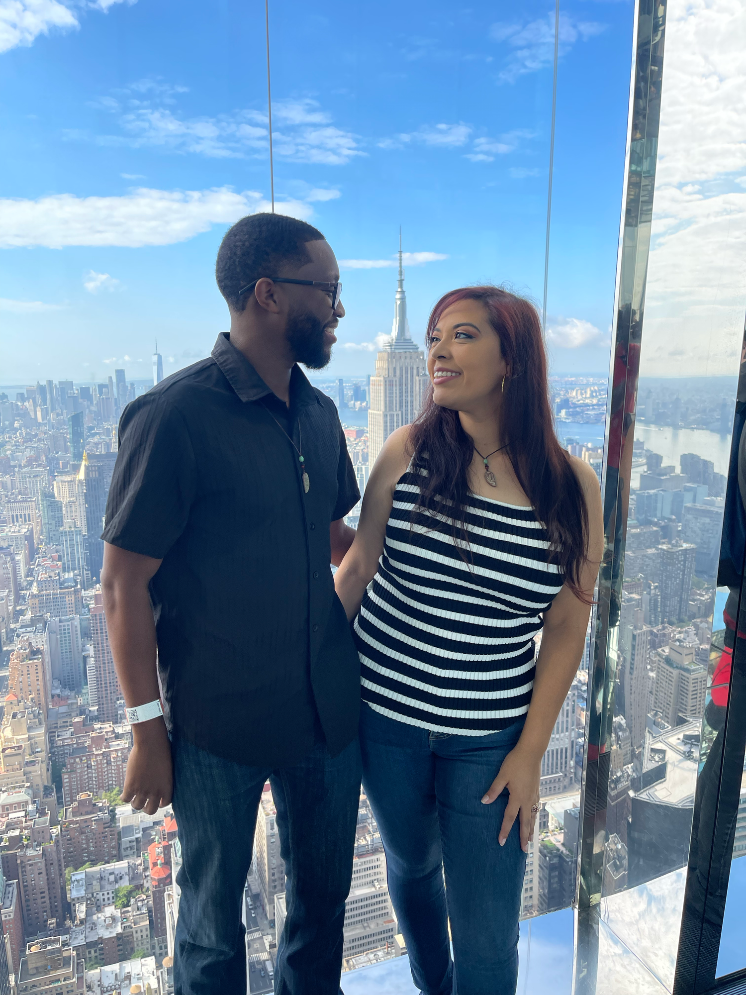 Couple smiling at each other on a high-rise observation deck with NYC skyline and Empire State Building behind them.