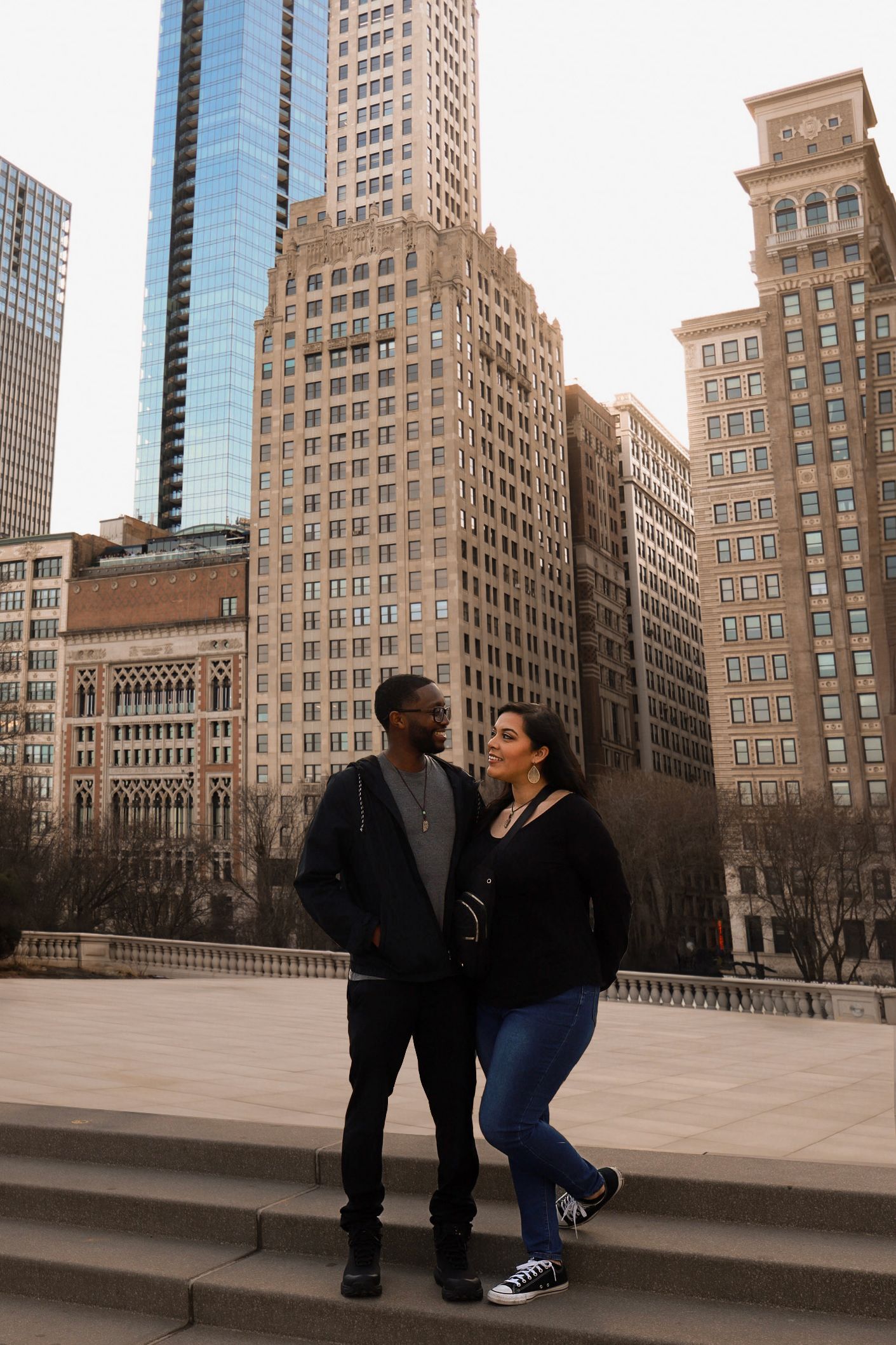 Couple standing together on steps with Chicago skyline and tall buildings in the background on a clear day.