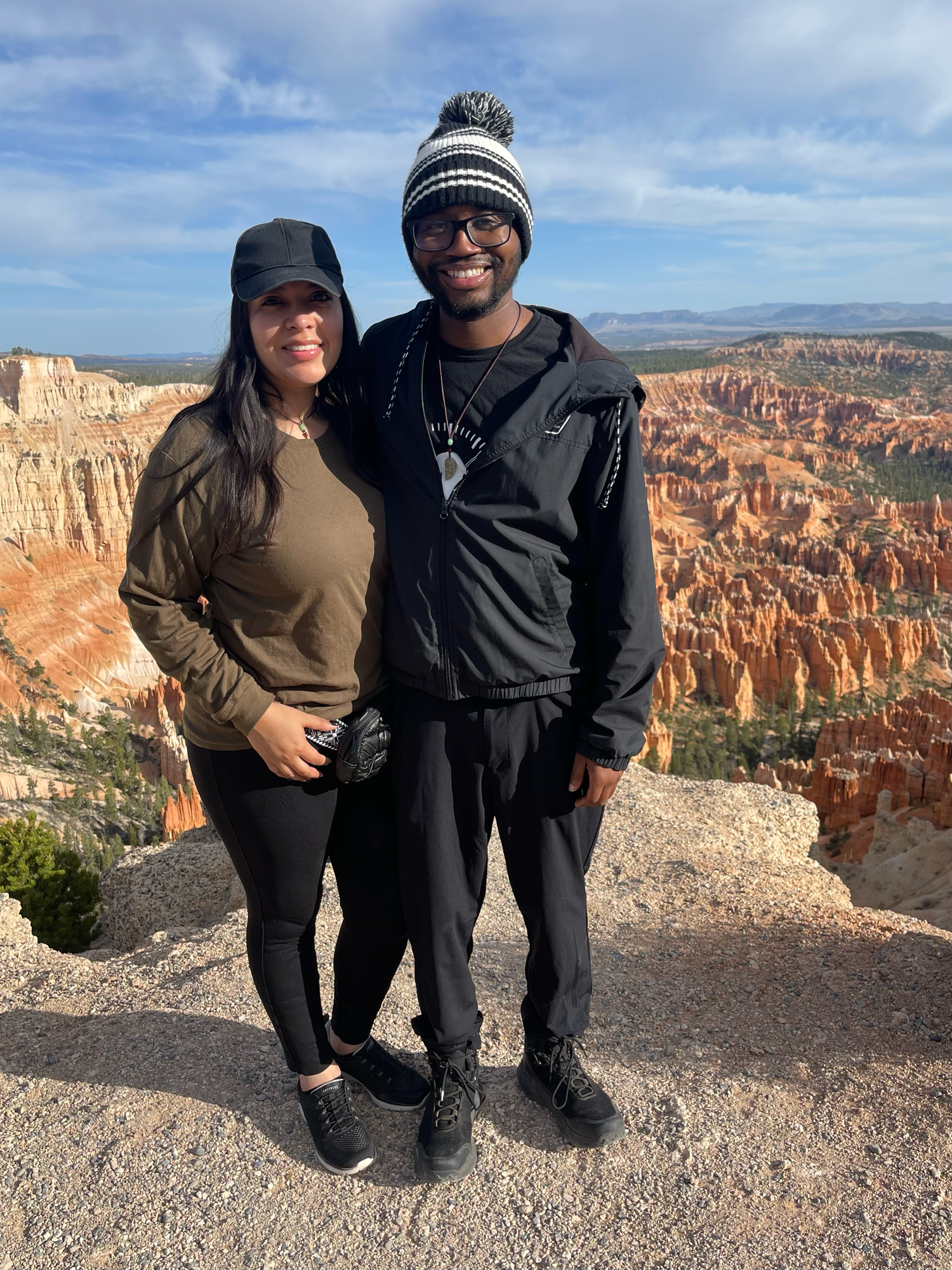 Couple smiling at Bryce Canyon National Park overlook, surrounded by red rock hoodoos under a blue sky.