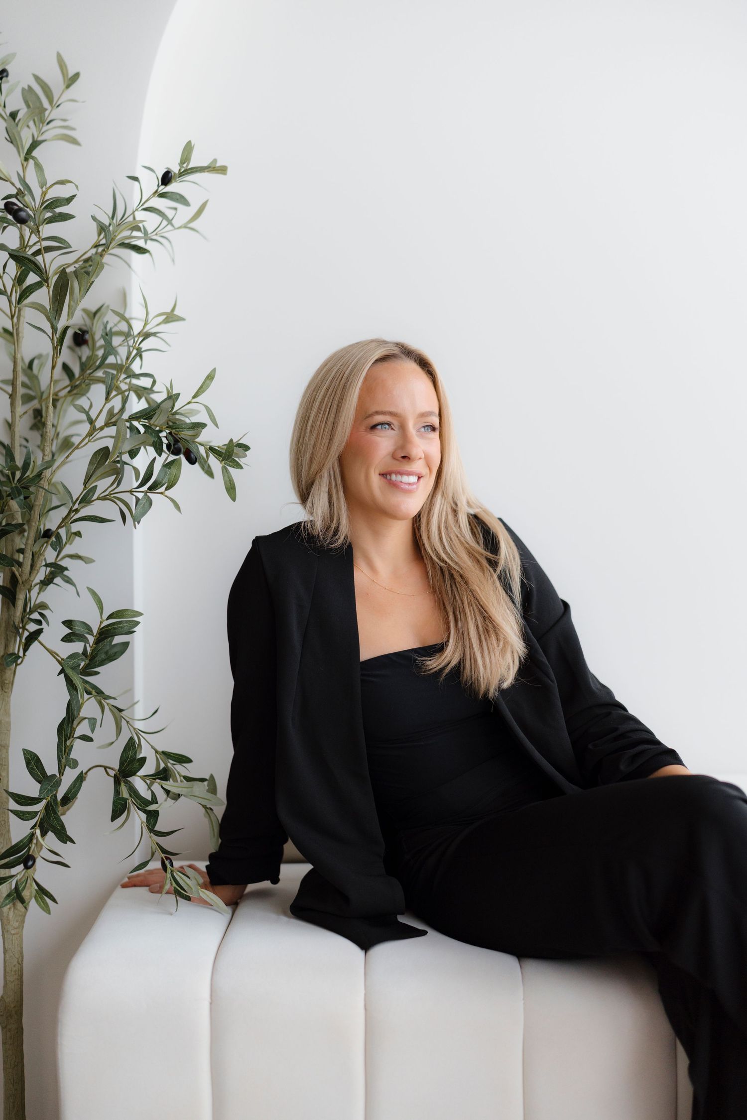 Professional portrait series showing a person in black attire posing on a white couch with green plants in the background.
