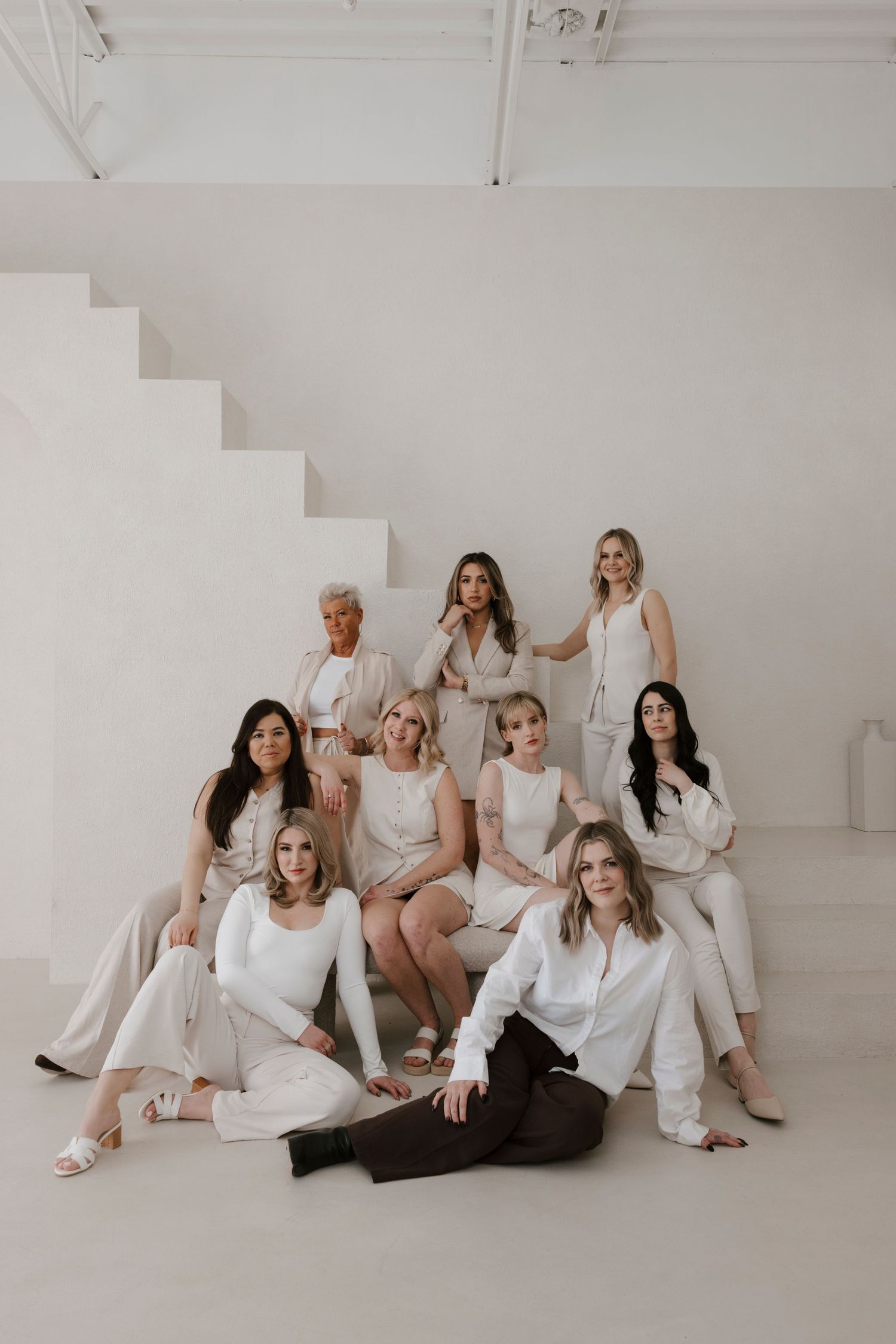 Group of people wearing white outfits pose together against a minimalist white studio backdrop.