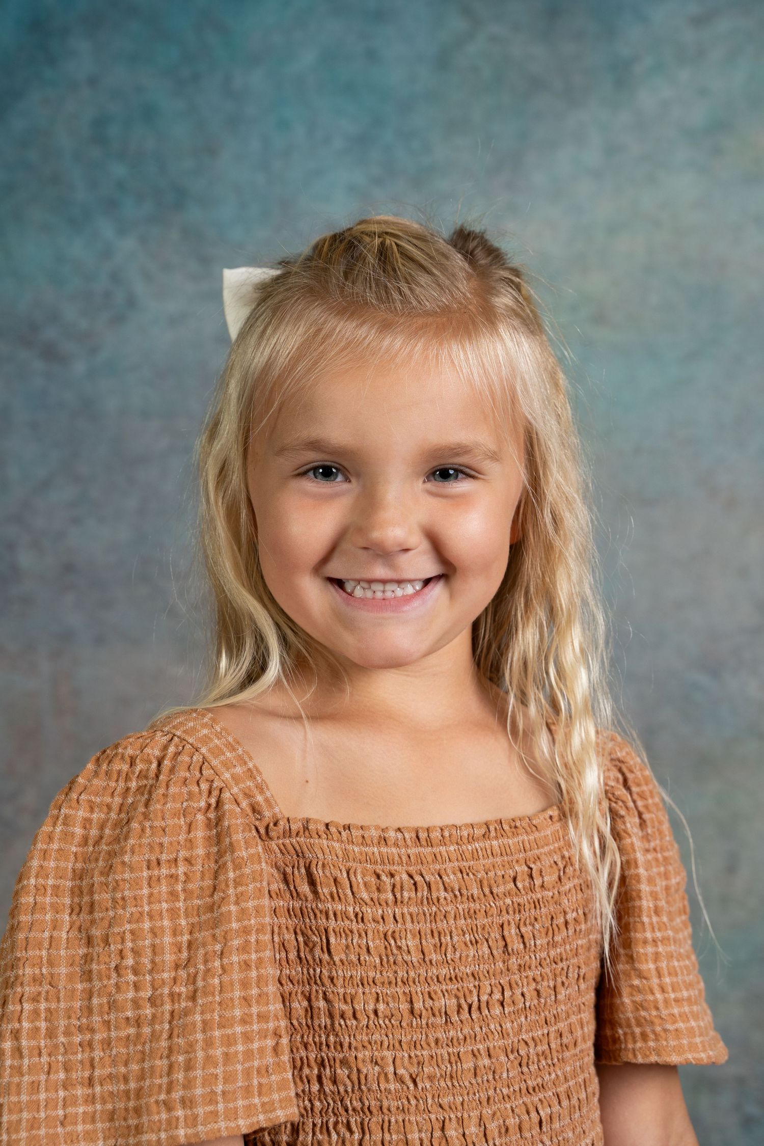 A series of four photos showing a child in a brown smocked top with blonde hair against a blue-gray backdrop.