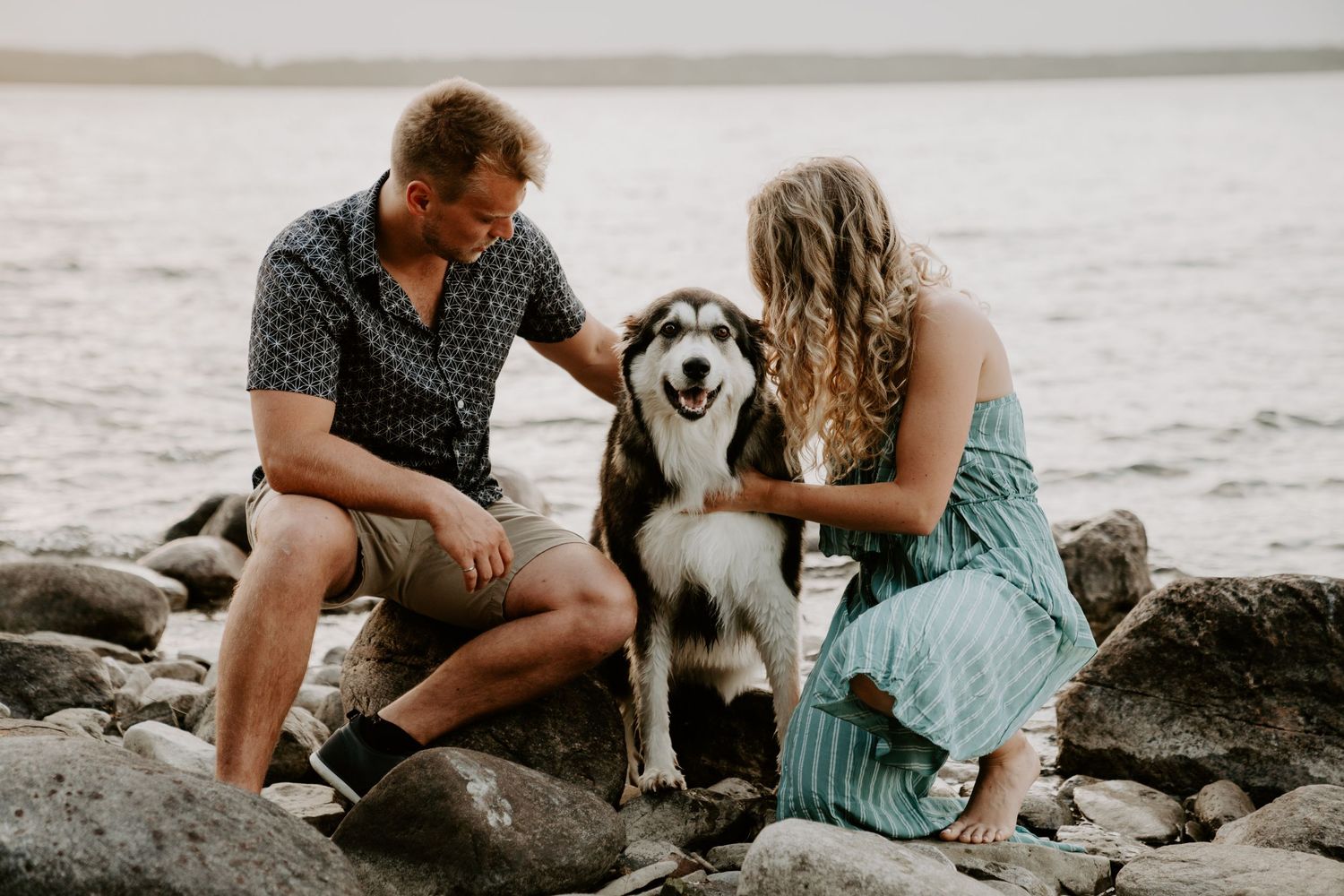 couple with their dog between them. dog is looking at the camera and couple is looking at dog