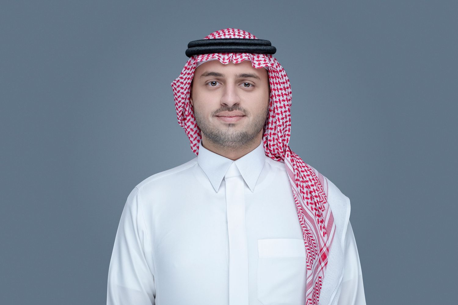 Person wearing traditional Middle Eastern white thobe and red and white checkered headdress against gray background.