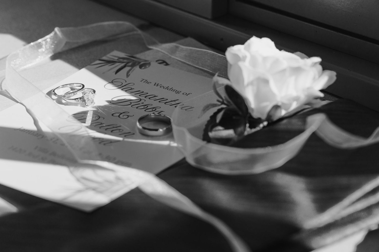 Black and white detail shot of wedding stationery with a white rose.