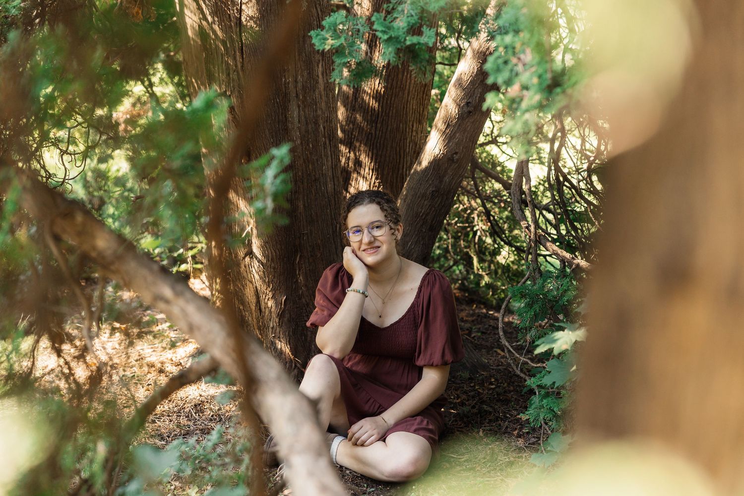 A person sits under trees with dappled sunlight filtering through the leaves.