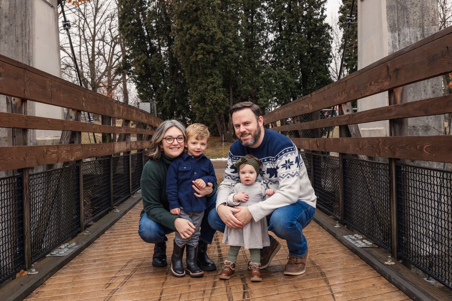 A family gathered on a wooden bridge surrounded by evergreen trees.