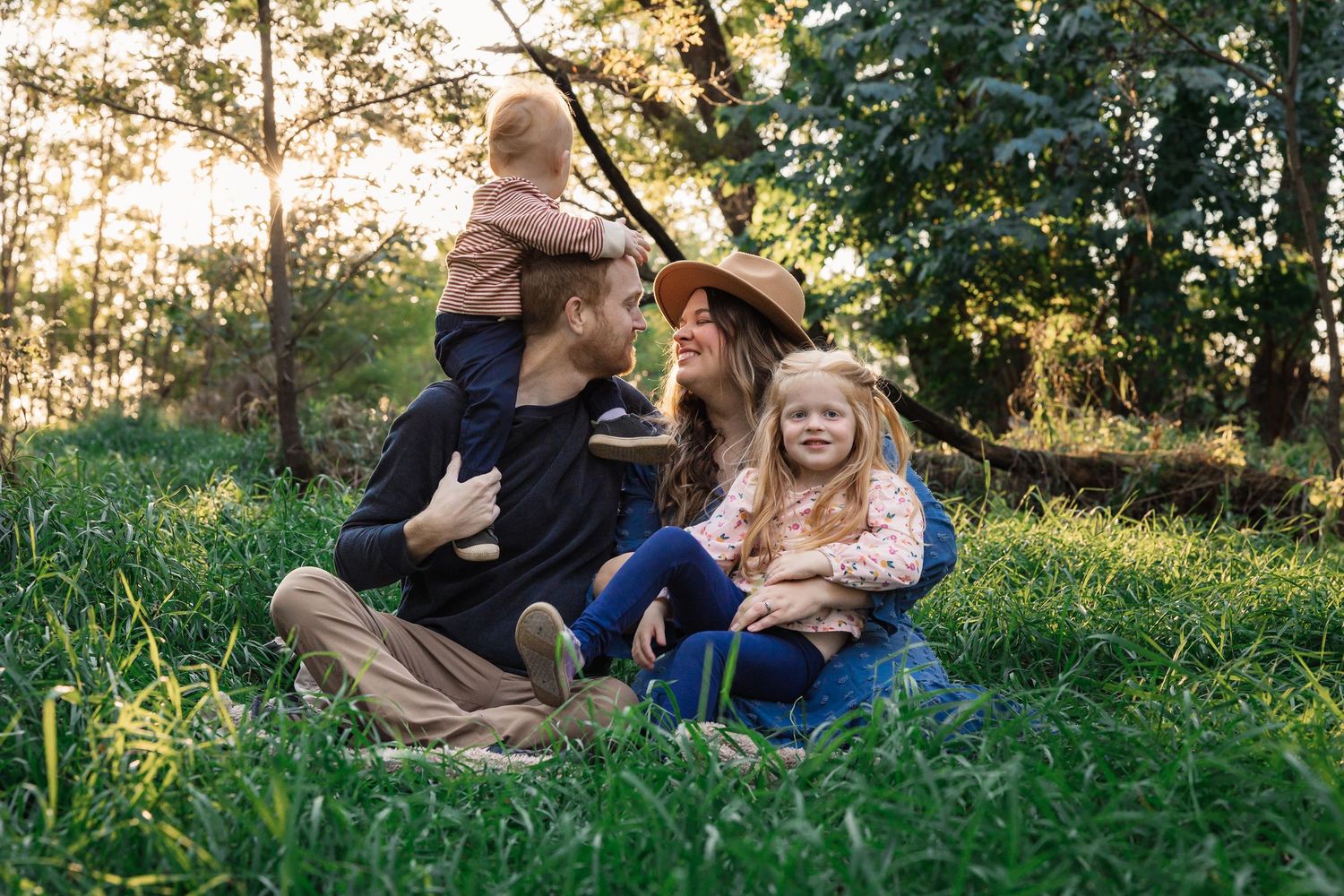A happy group rests together on green grass during golden sunset hour in a natural outdoor setting.