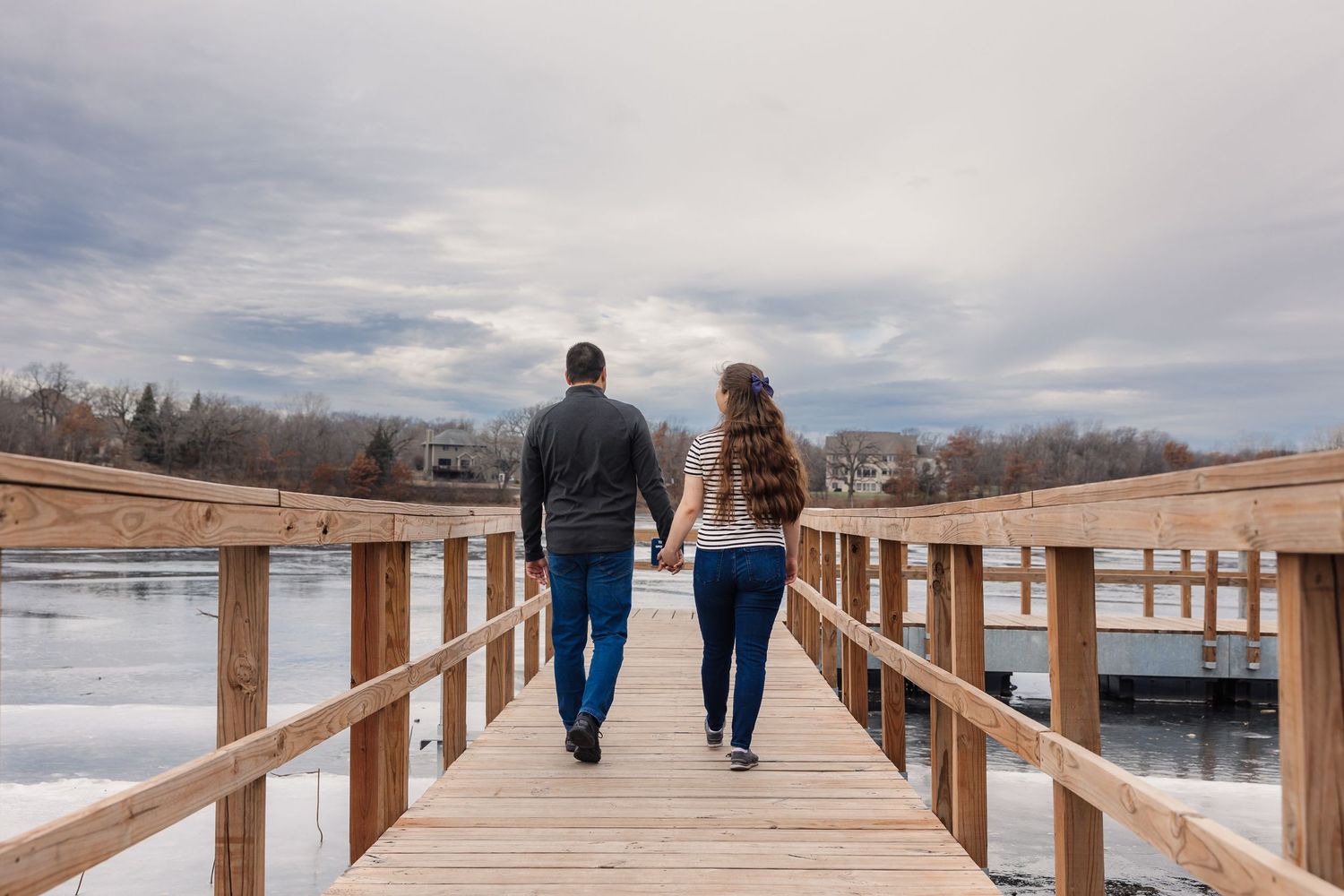 Two people walk together on a wooden boardwalk over a frozen lake.