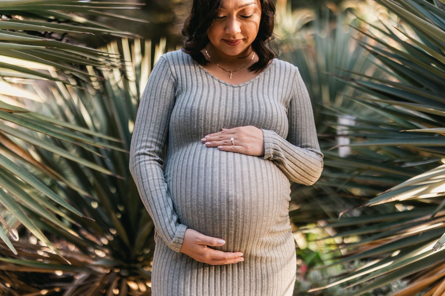 Close-up maternity portrait with palm fronds showing woman in grey ribbed dress.
