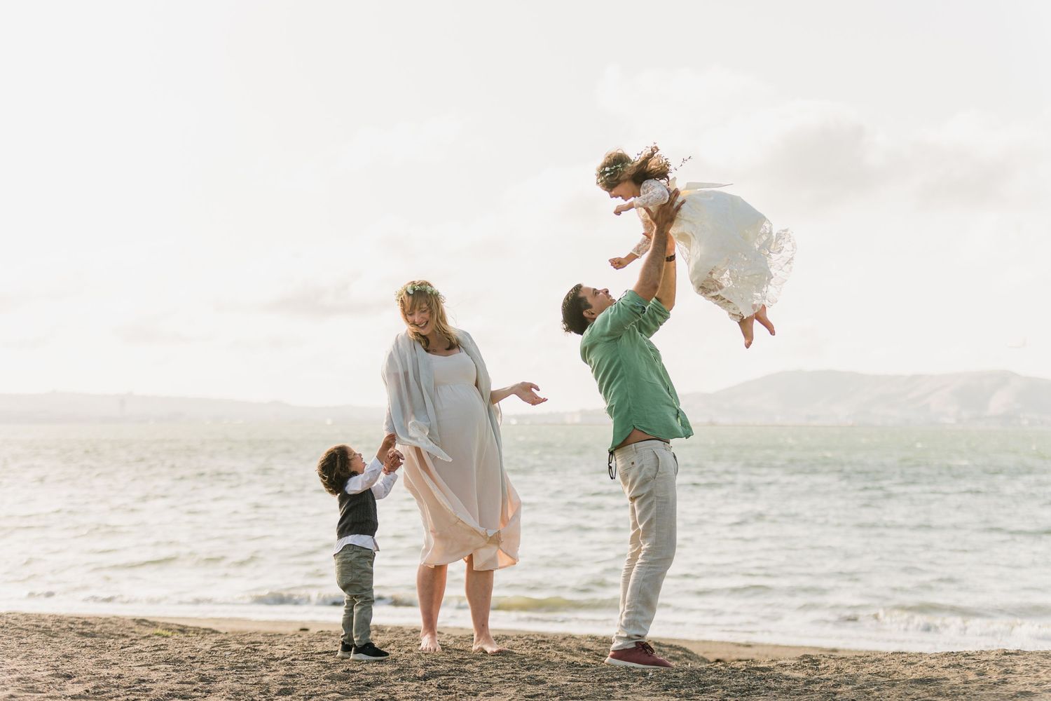 A joyful family moment on the beach at sunset with waves in the background.