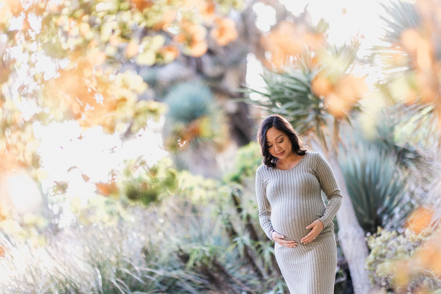 Artistic maternity photo with dreamy bokeh effect and natural garden backdrop.