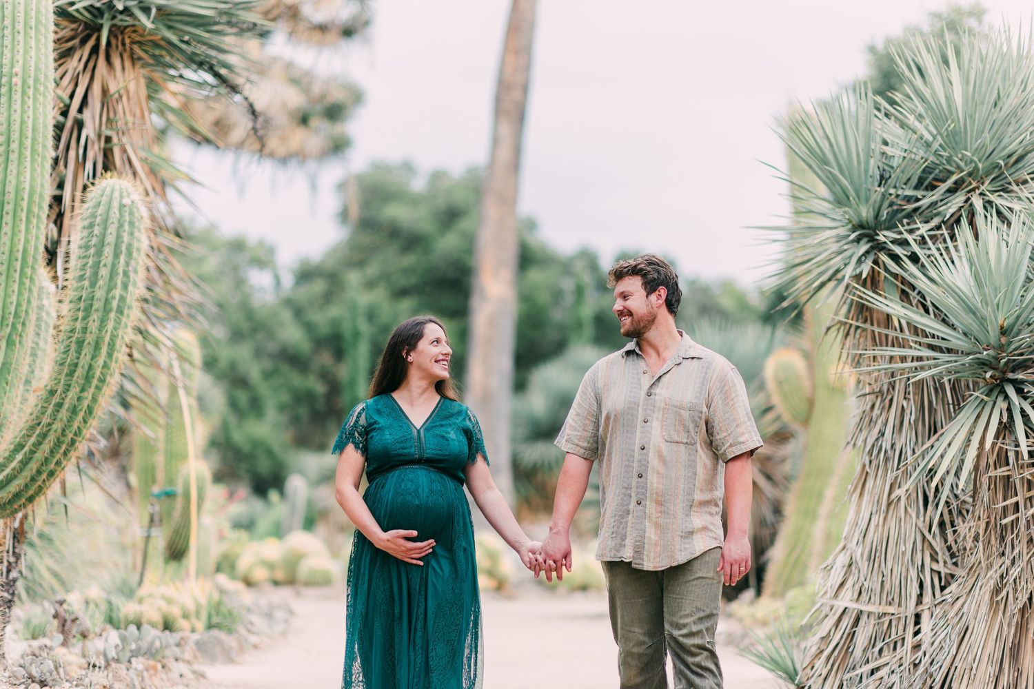 A couple walks hand in hand through a garden filled with desert plants and cacti.