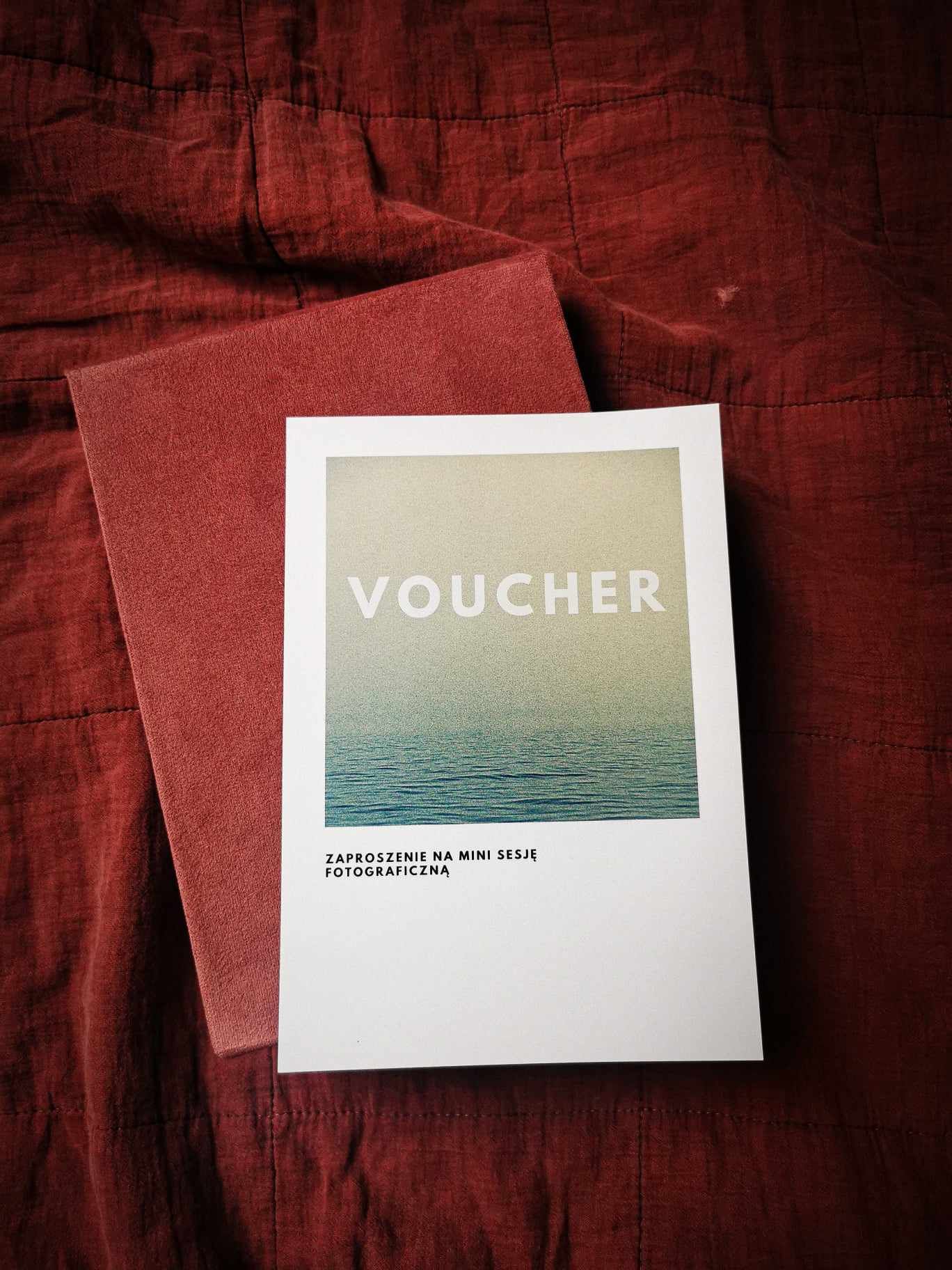 A photography session voucher with ocean design displayed on red fabric background.