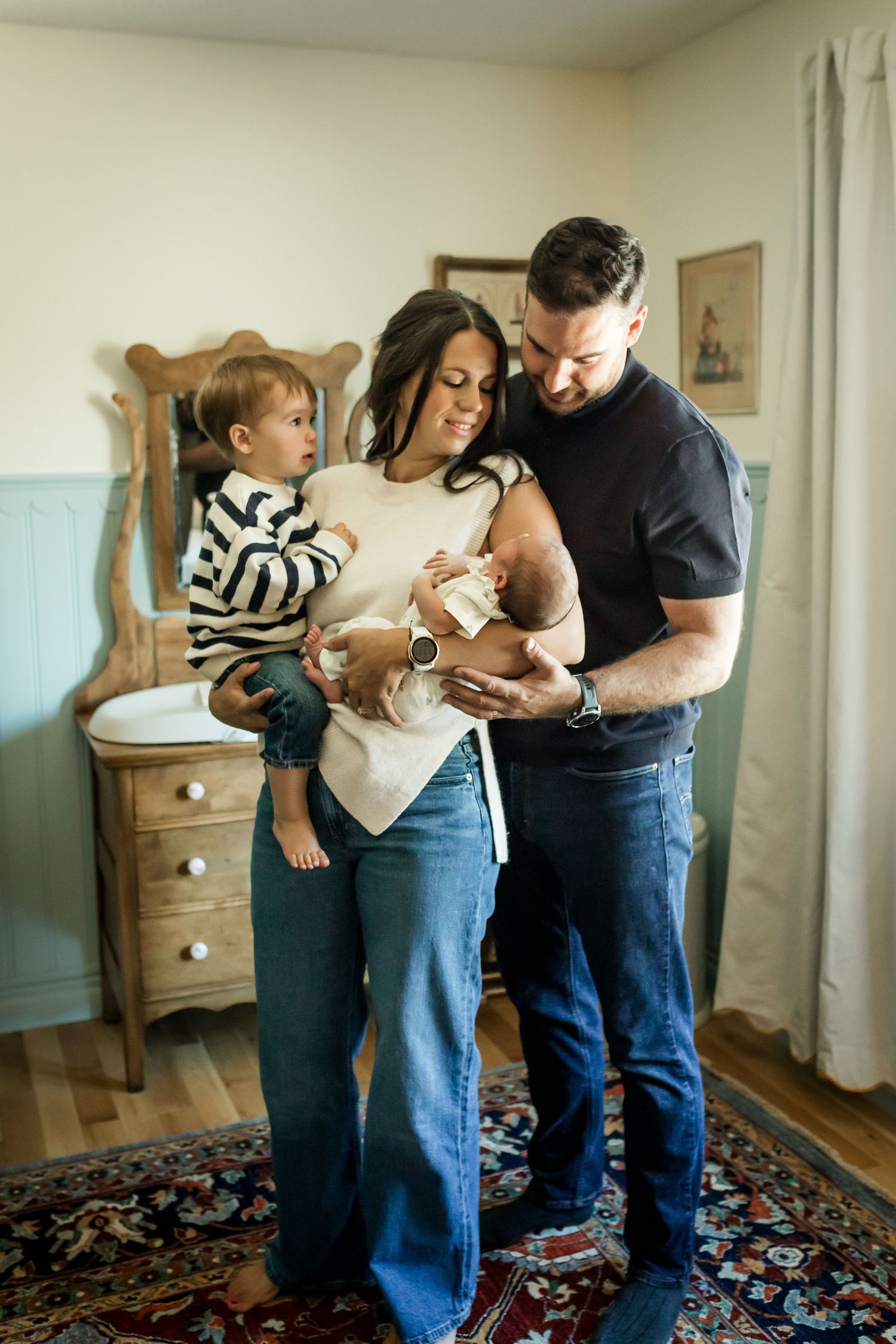 Calgary family standing in nursery and cuddling new baby during in-home lifestyle newborn photography session.