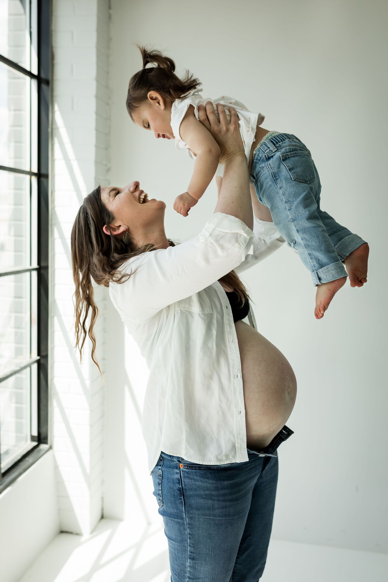 Expecting mother and young daughter playing and laughing in a studio at motherhood photography sessions in Calgary