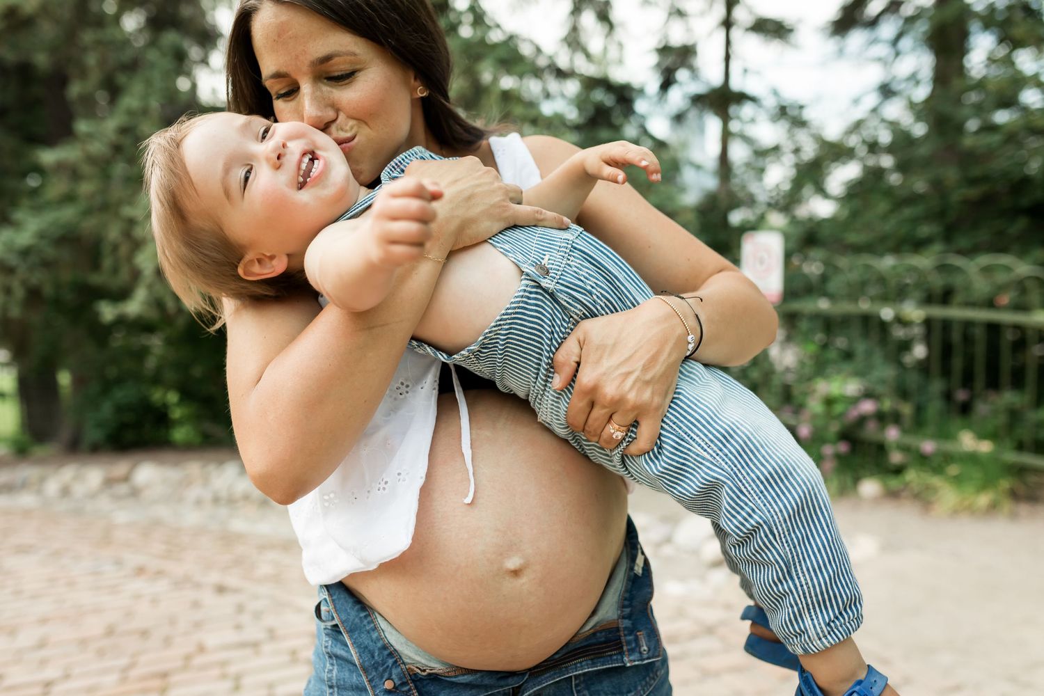 Pregnant mother and toddler laughing and playing during lifestyle maternity family photos in Calgary during summer.
