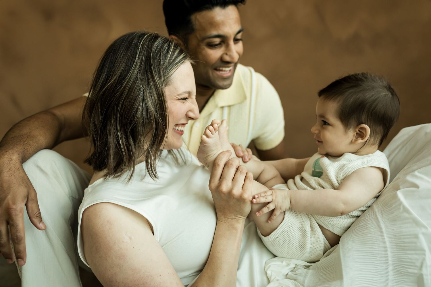 Mother tickling baby's feet while father laughs at a studio lifestyle family photography session in Calgary
