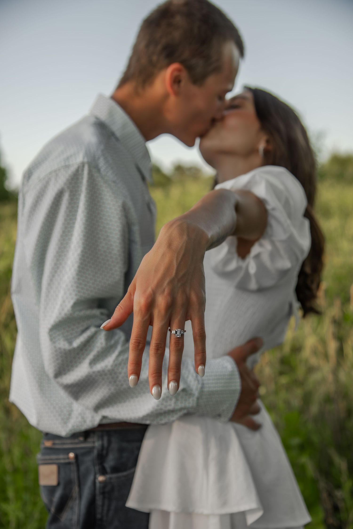 Intimate couple pose showing engagement ring detail against a natural outdoor background.