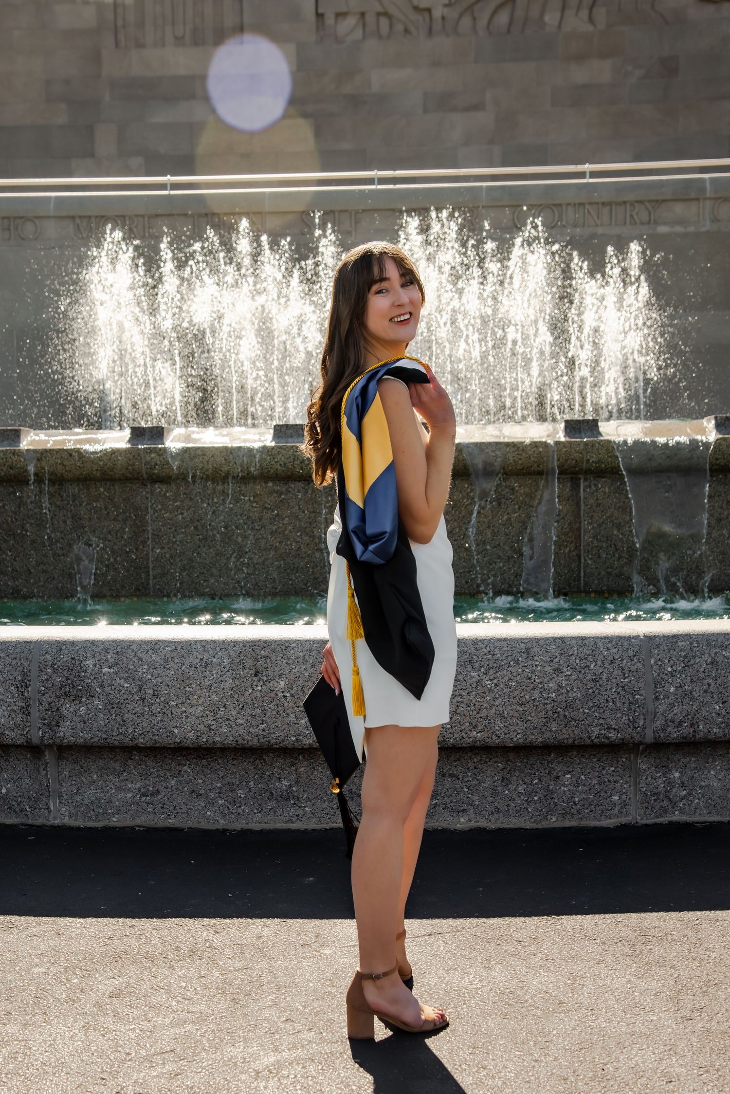 Graduation portrait session featuring casual poses near a modern water wall feature.
