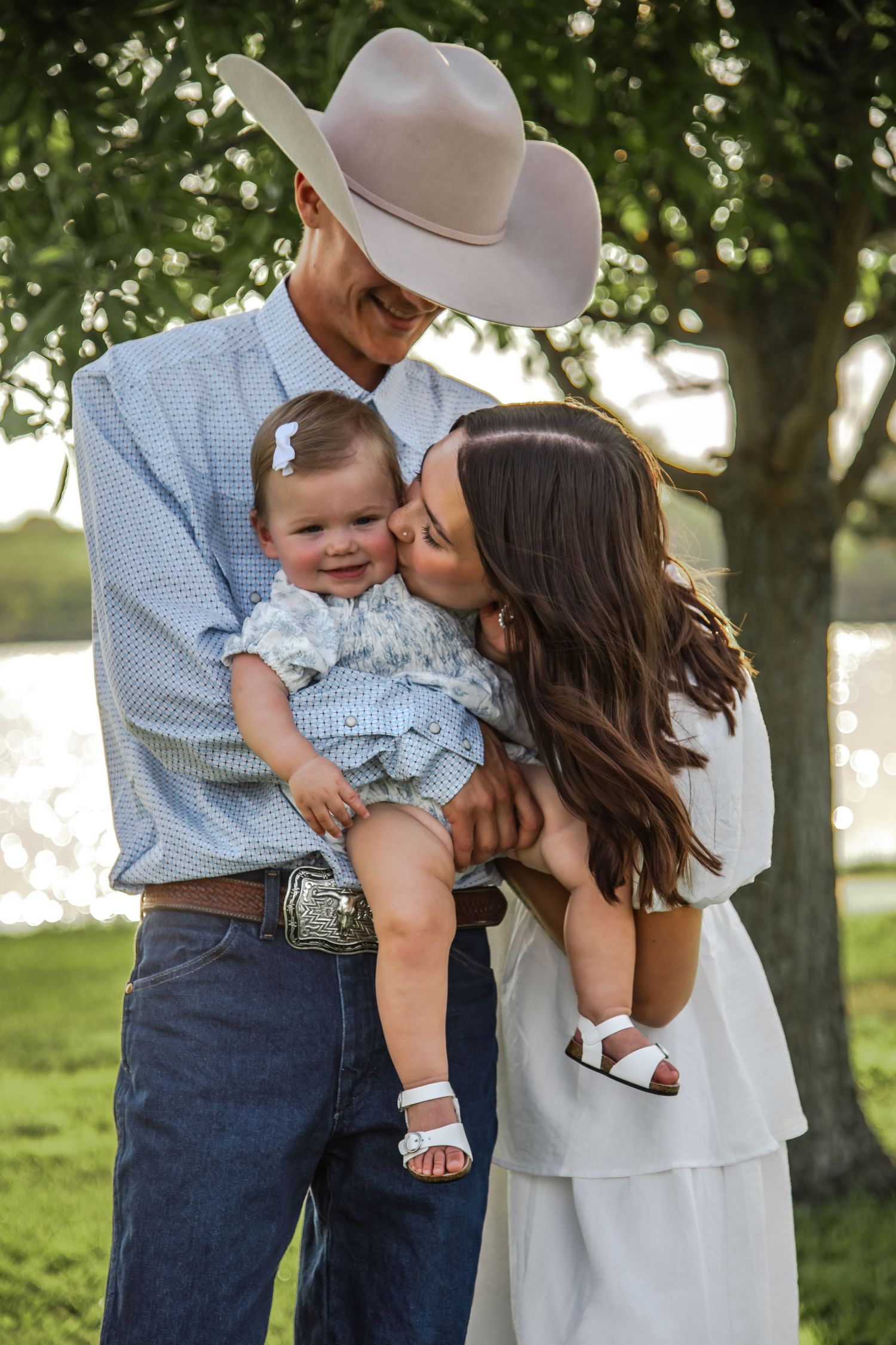 A family shares tender moments in a pastoral setting wearing coordinated blue and white country western outfits.
