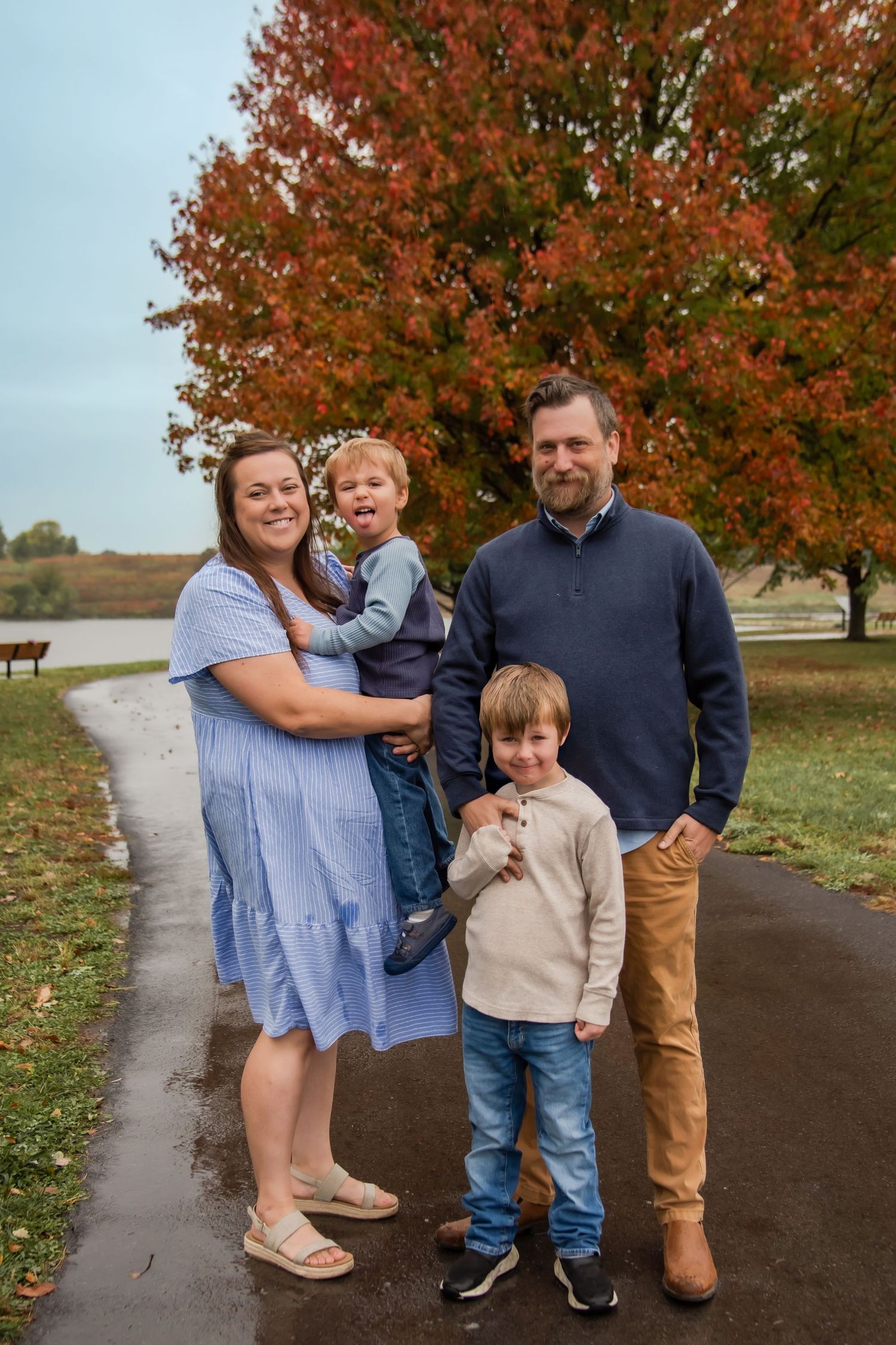 A family poses together on an autumn path with vibrant orange trees in the background.