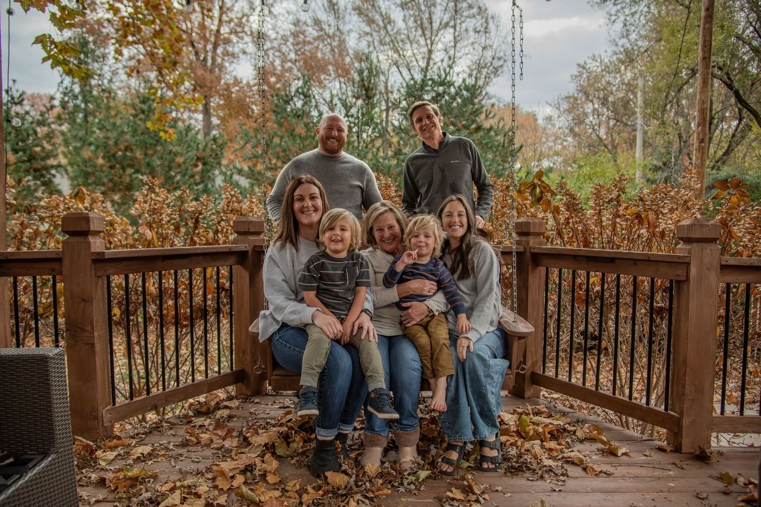 Outdoor autumn photo session on wooden deck with fall leaves and natural scenery in background.