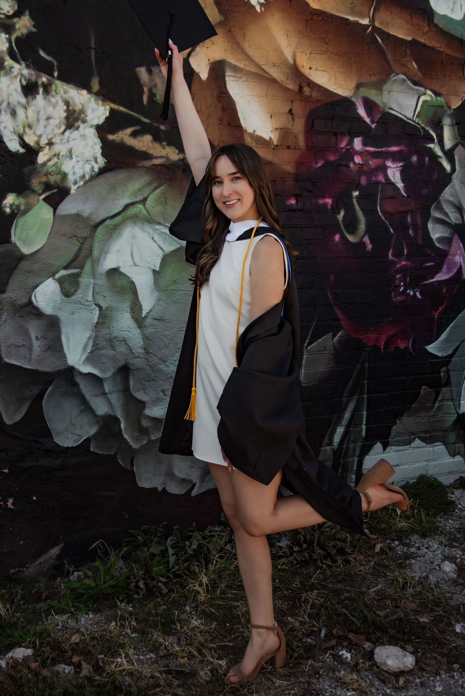 Graduate in academic regalia poses against floral backdrop with purple lighting.