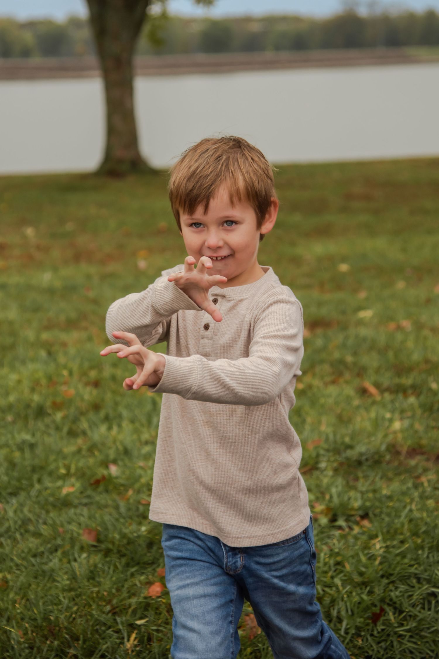 Child in casual attire making playful dance moves on grassy field with trees in background.