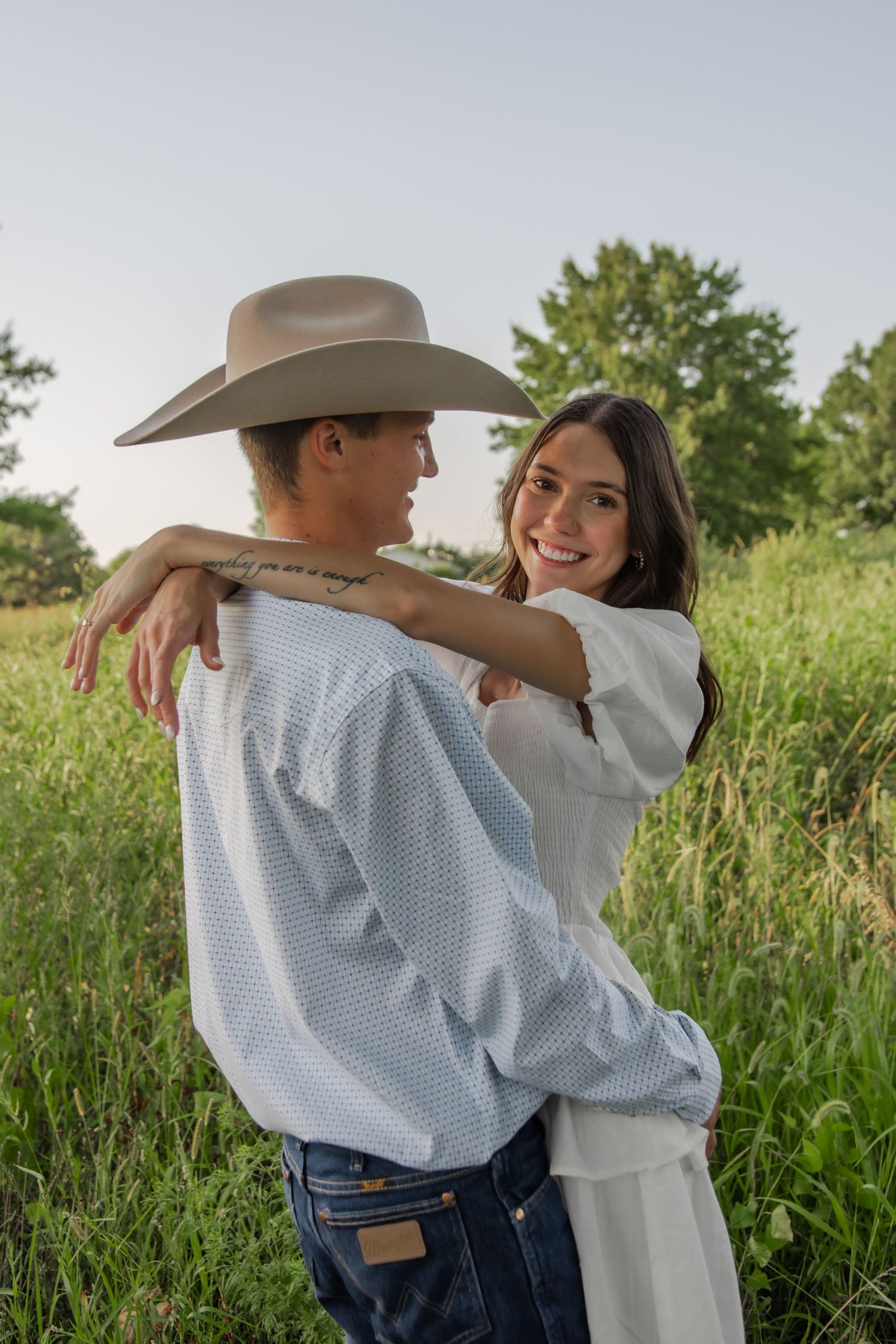 A romantic embrace between couple in western attire against grassy field background.