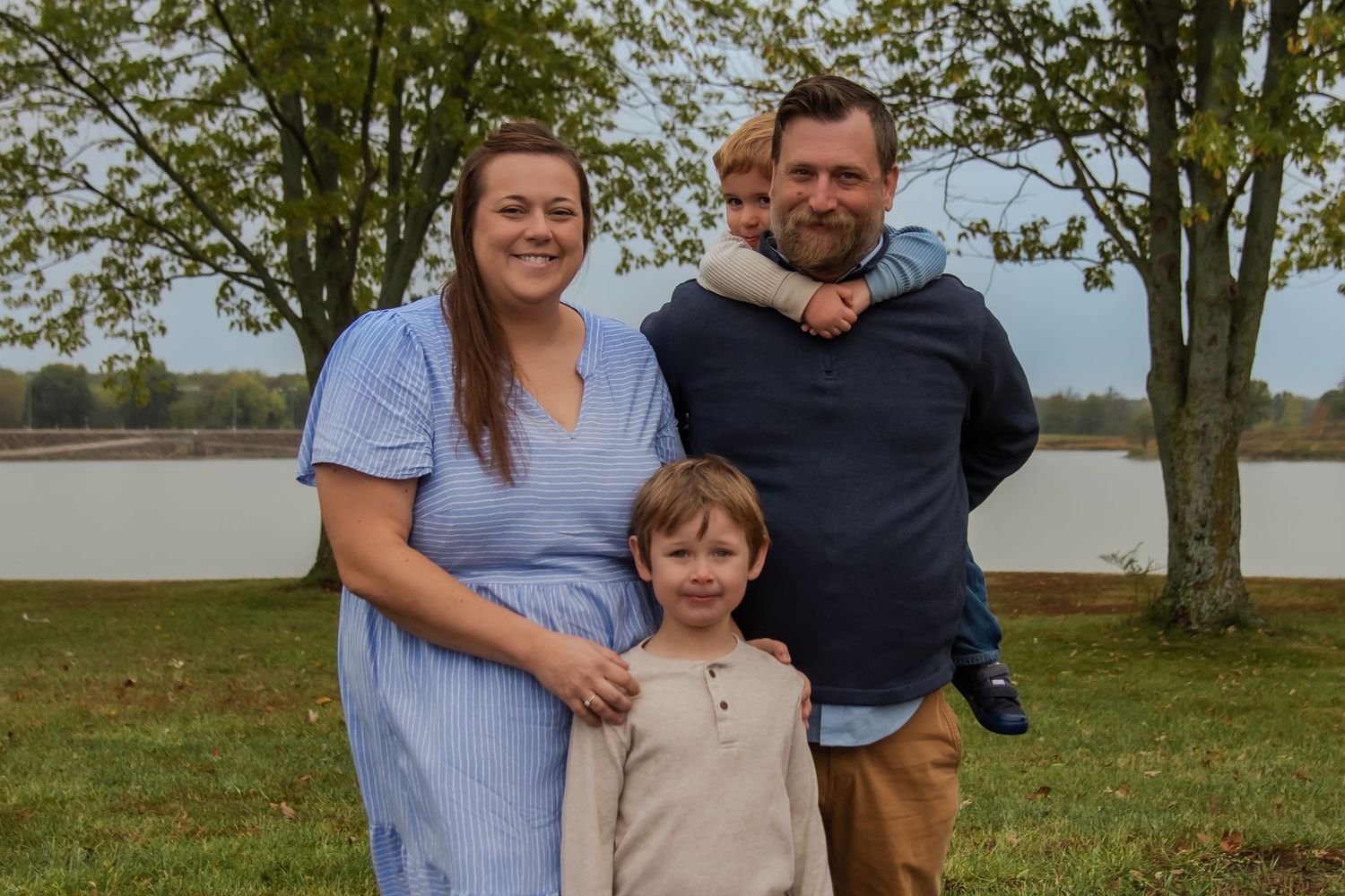 A family poses together outdoors on a grassy field near trees on an autumn day.