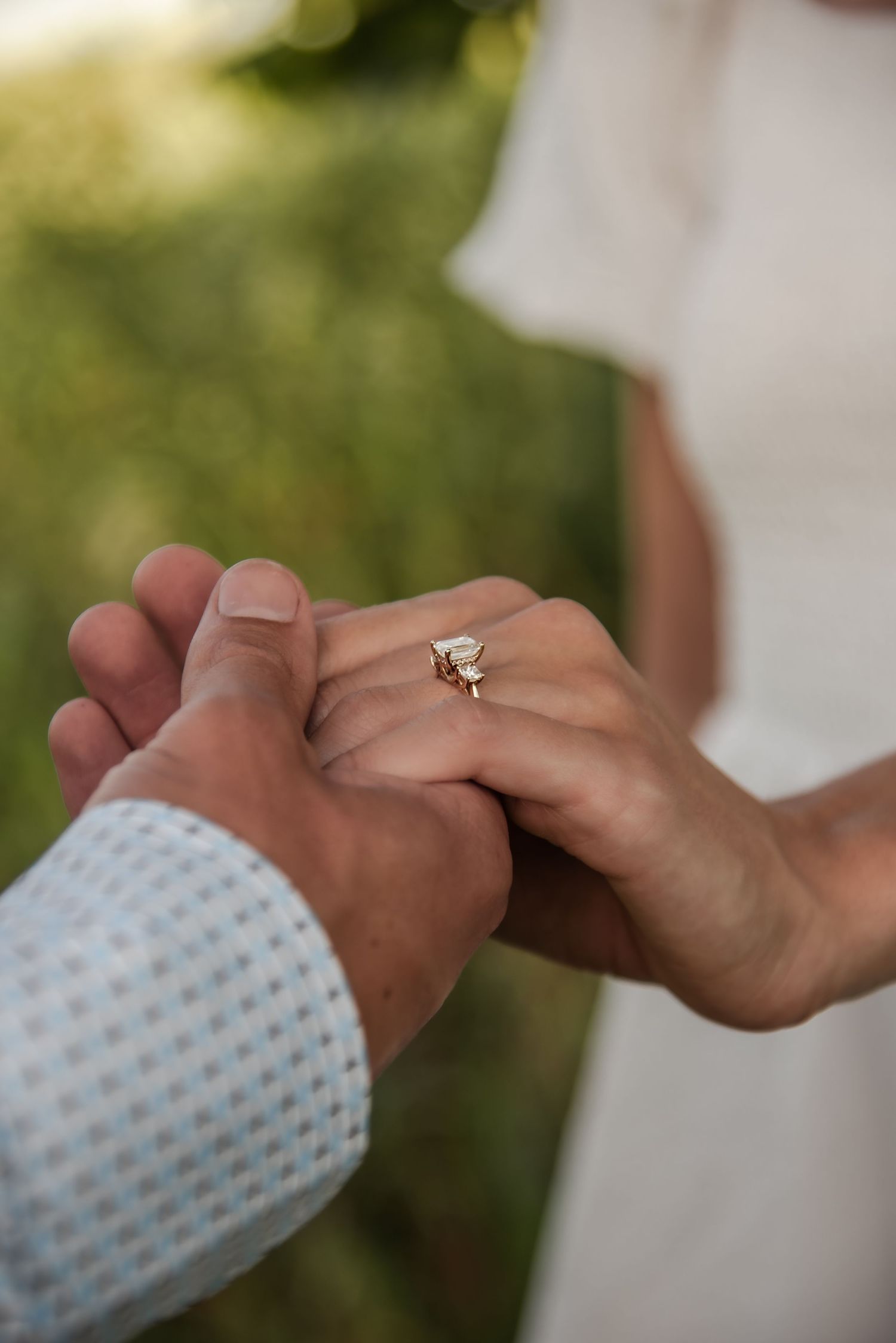 Two people holding hands with one wearing a blue and white polka dot sleeve, showing engagement rings against a blurred background.
