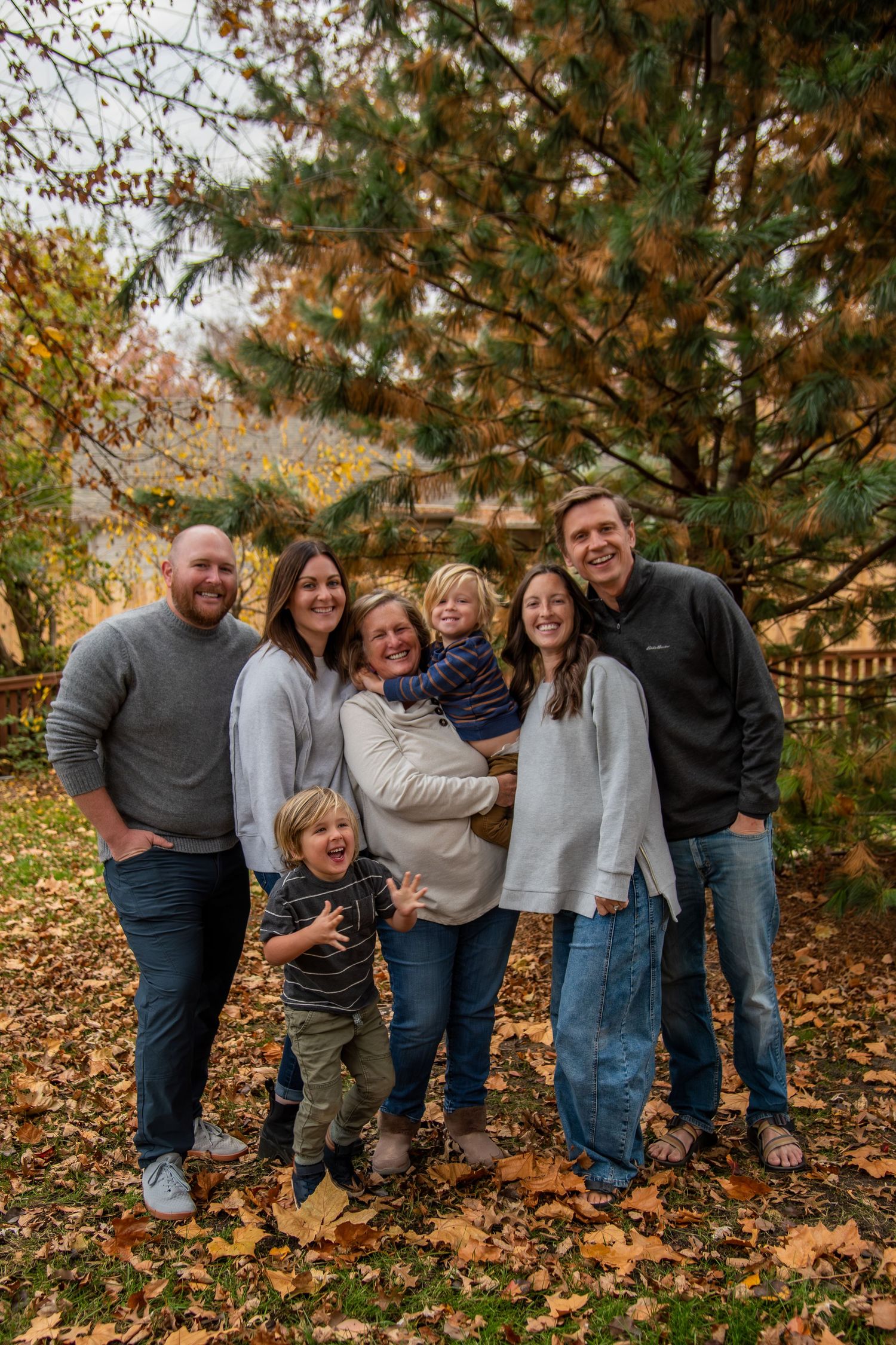A group stands together outdoors on an autumn day with fallen leaves and trees in the background.