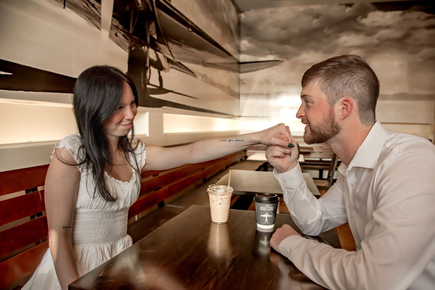 A couple sits at a bar counter sharing a milkshake with two straws in a romantic vintage-style setting.