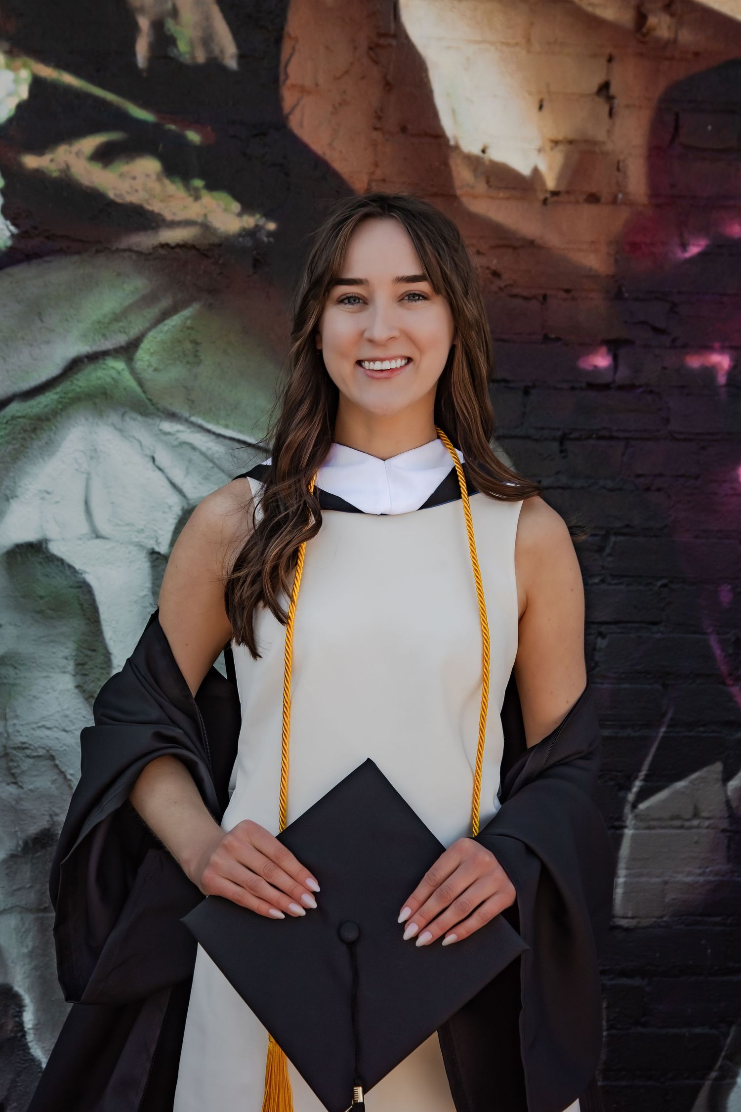 Graduate in academic regalia poses against artistic wall mural.
