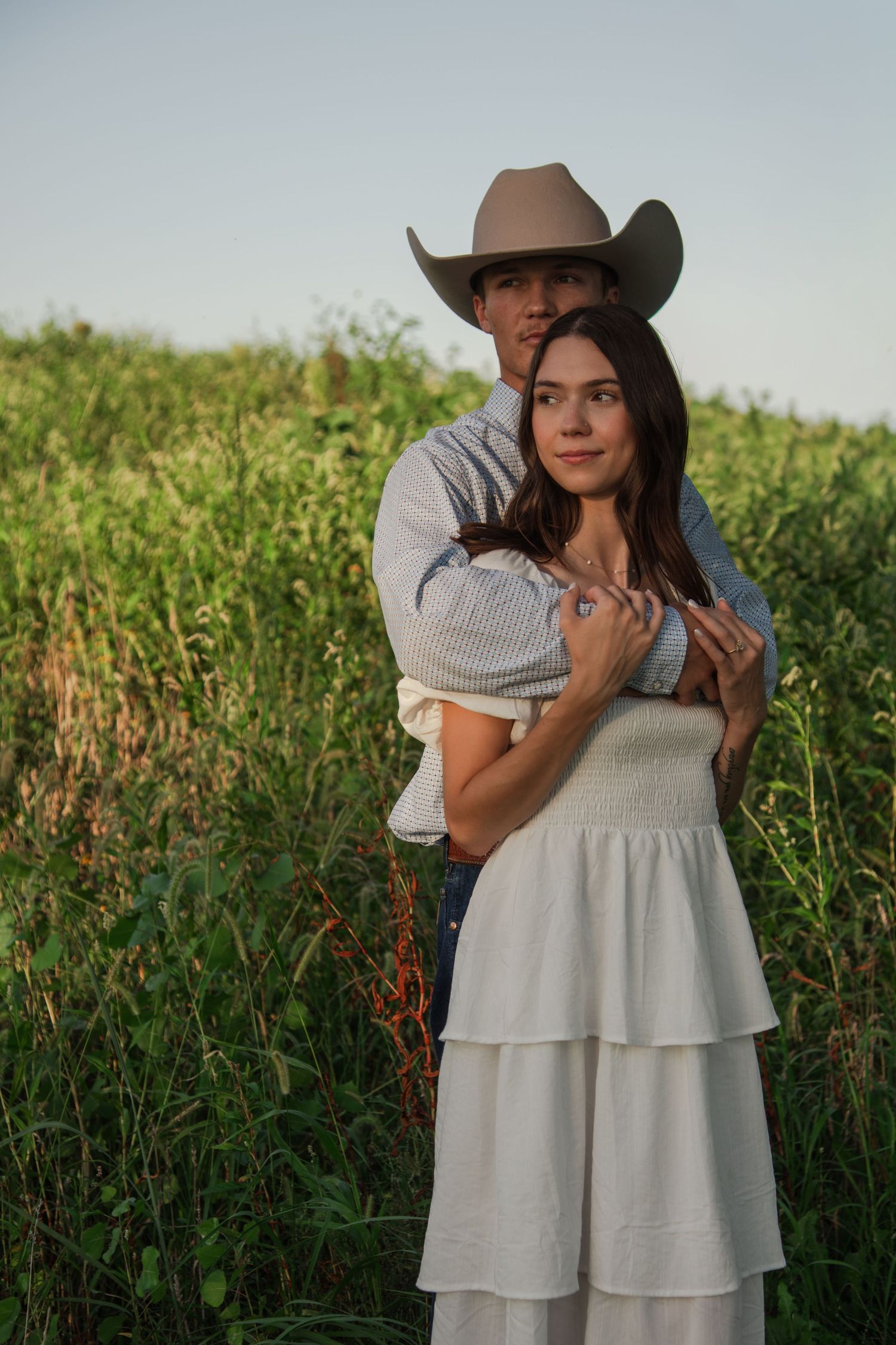 A couple in rustic country attire shares intimate moments in a sunlit meadow.